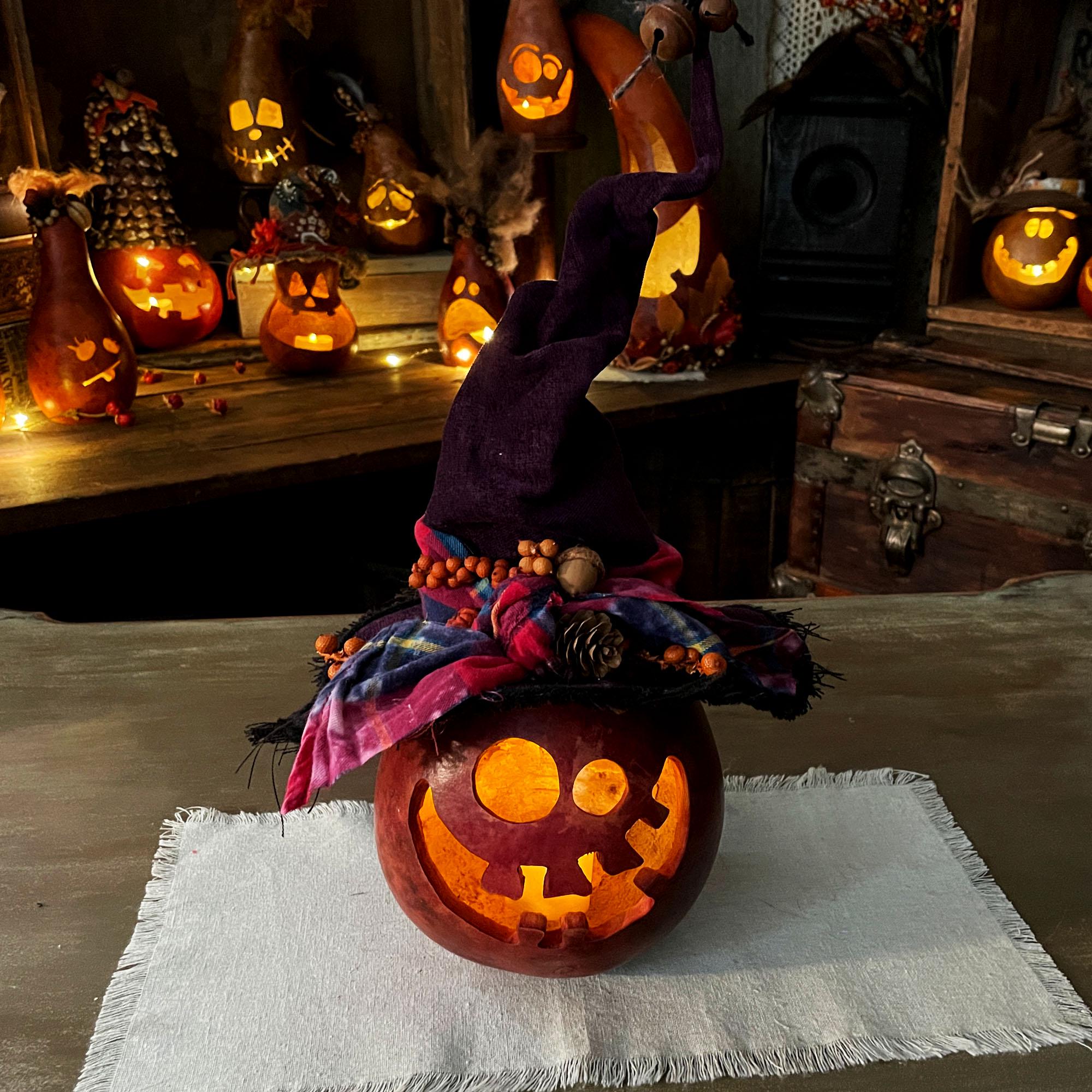 Decorative Halloween pumpkin with a witch hat on a tablecloth, surrounded by more pumpkins and decorations.
