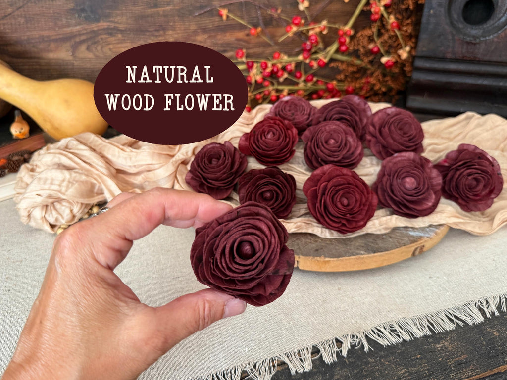 Maroon wood flowers on a wooden stand with a hand holding one, against a rustic background.