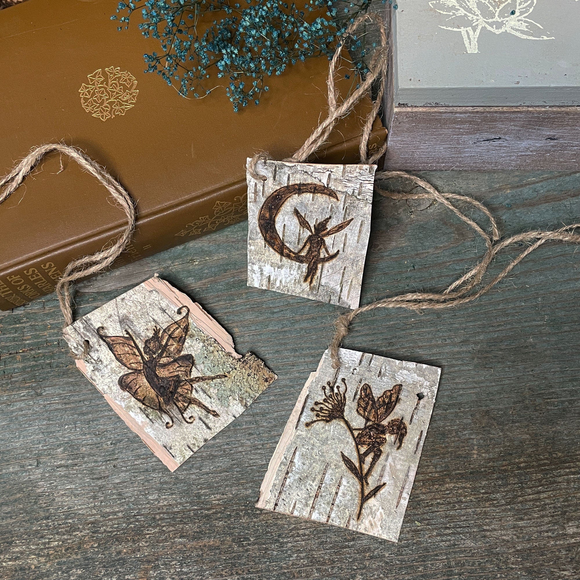 Three wooden tags with fairy designs hanging on a string against a rustic background.