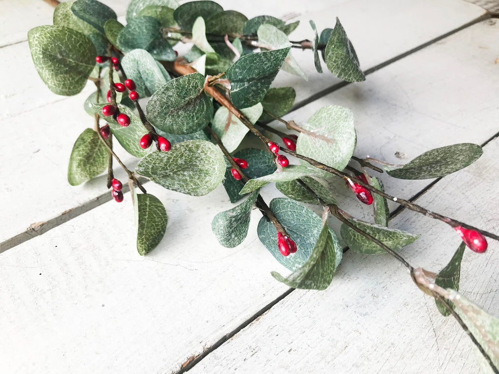 Green leaves with red berries on a light wooden surface