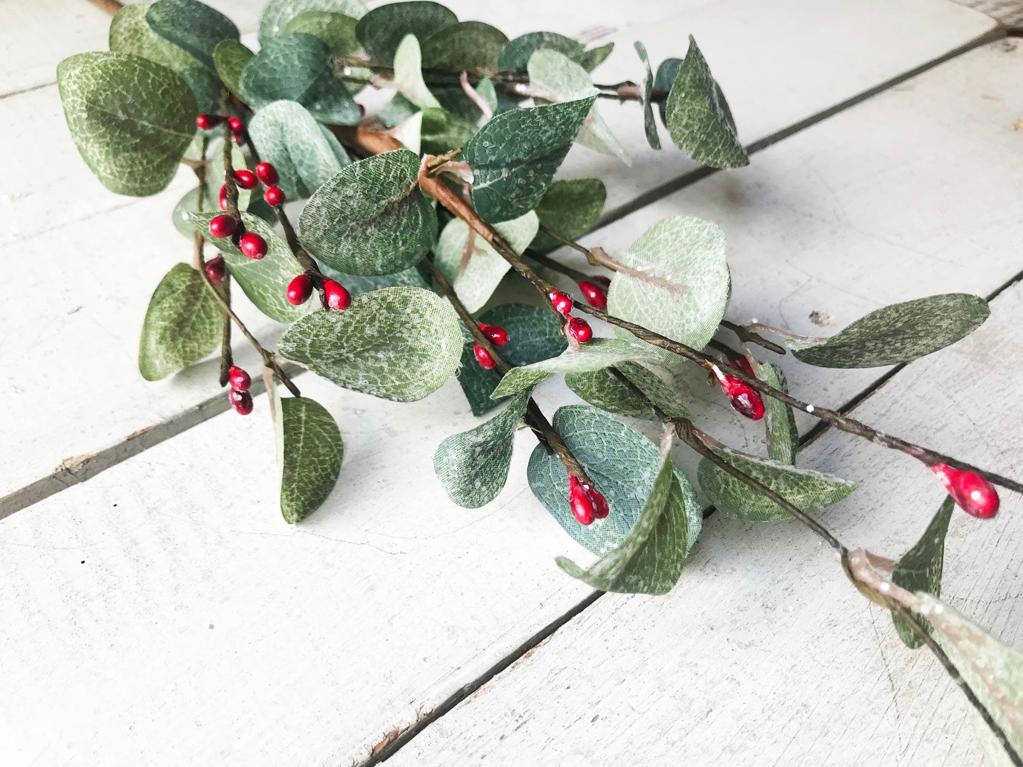Green leaves with red berries on a light wooden surface