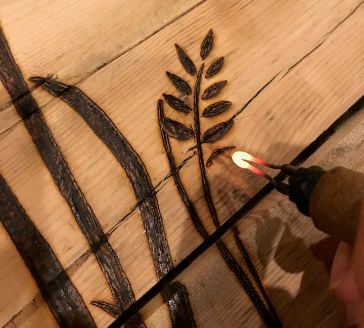 Person using a lighter to draw on a wooden surface with black ink.