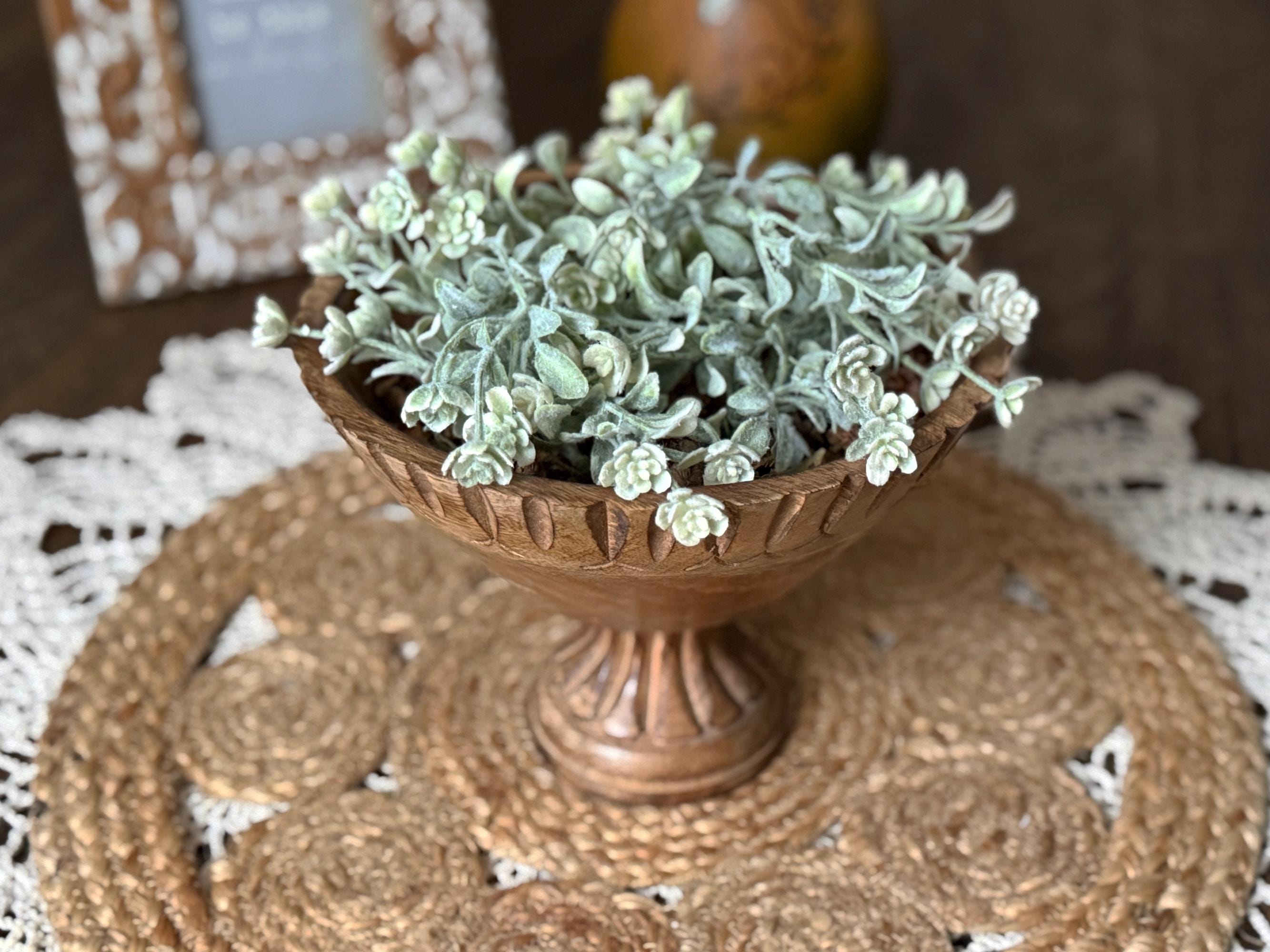 Decorative teak wood bowl with a soft greenery arrangement in it.