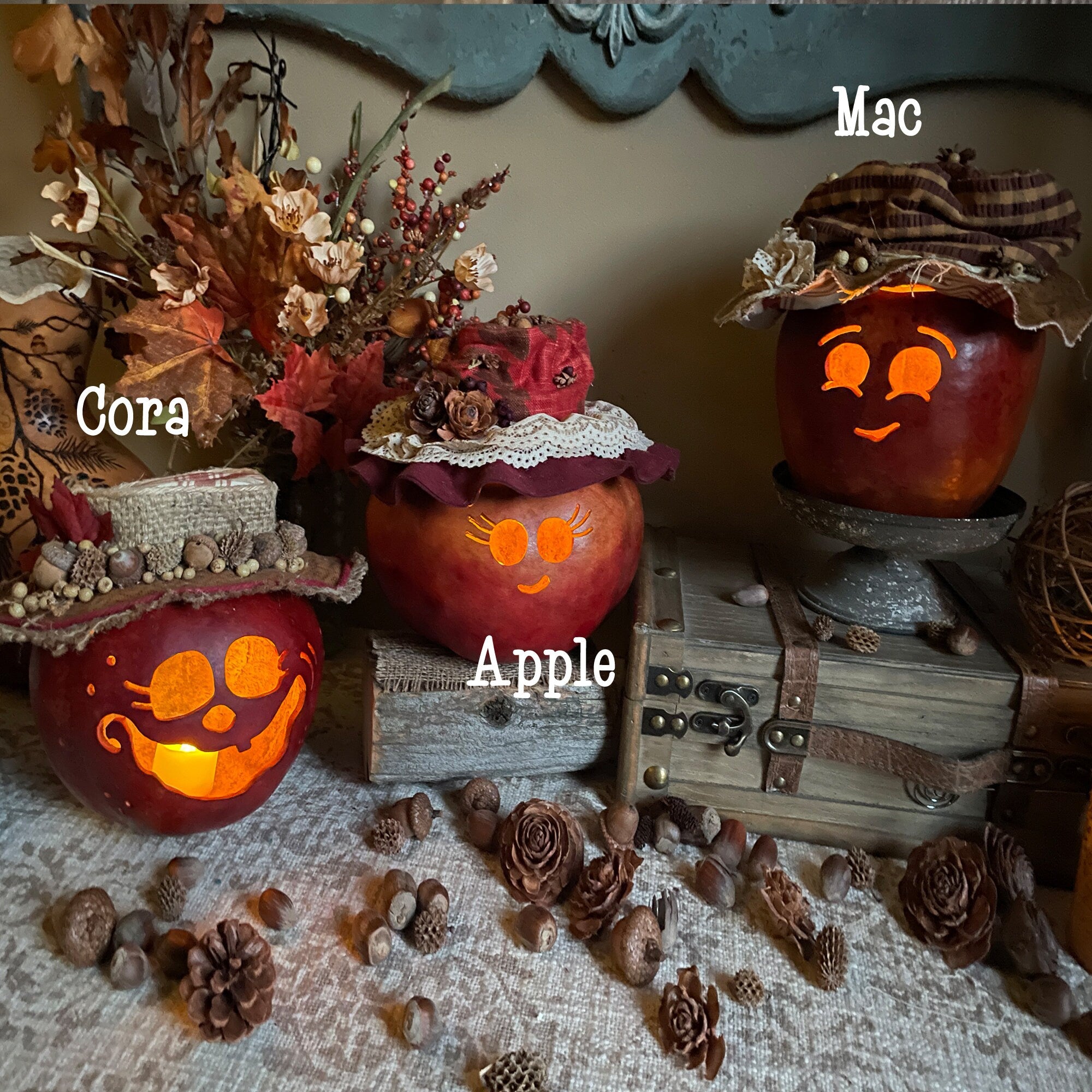 Three carved pumpkins with decorative hats on a lace tablecloth with pinecones and flowers.