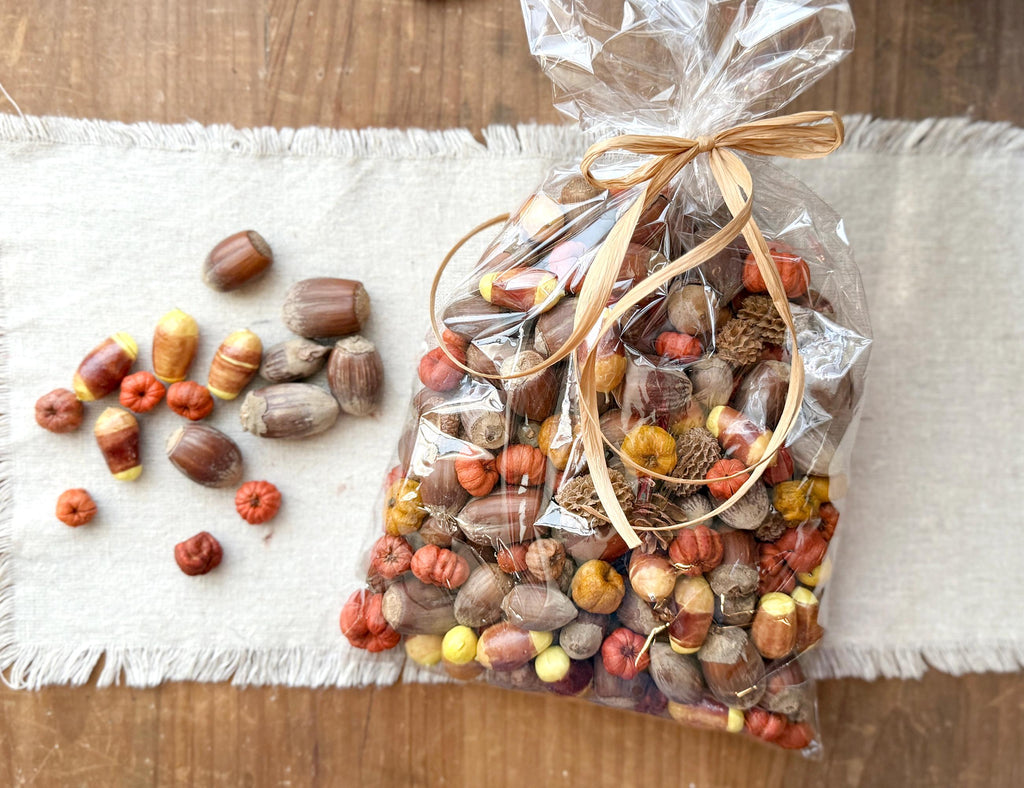 Decorative bag of assorted fall bowl fillers on a wooden surface with a white cloth underneath.
