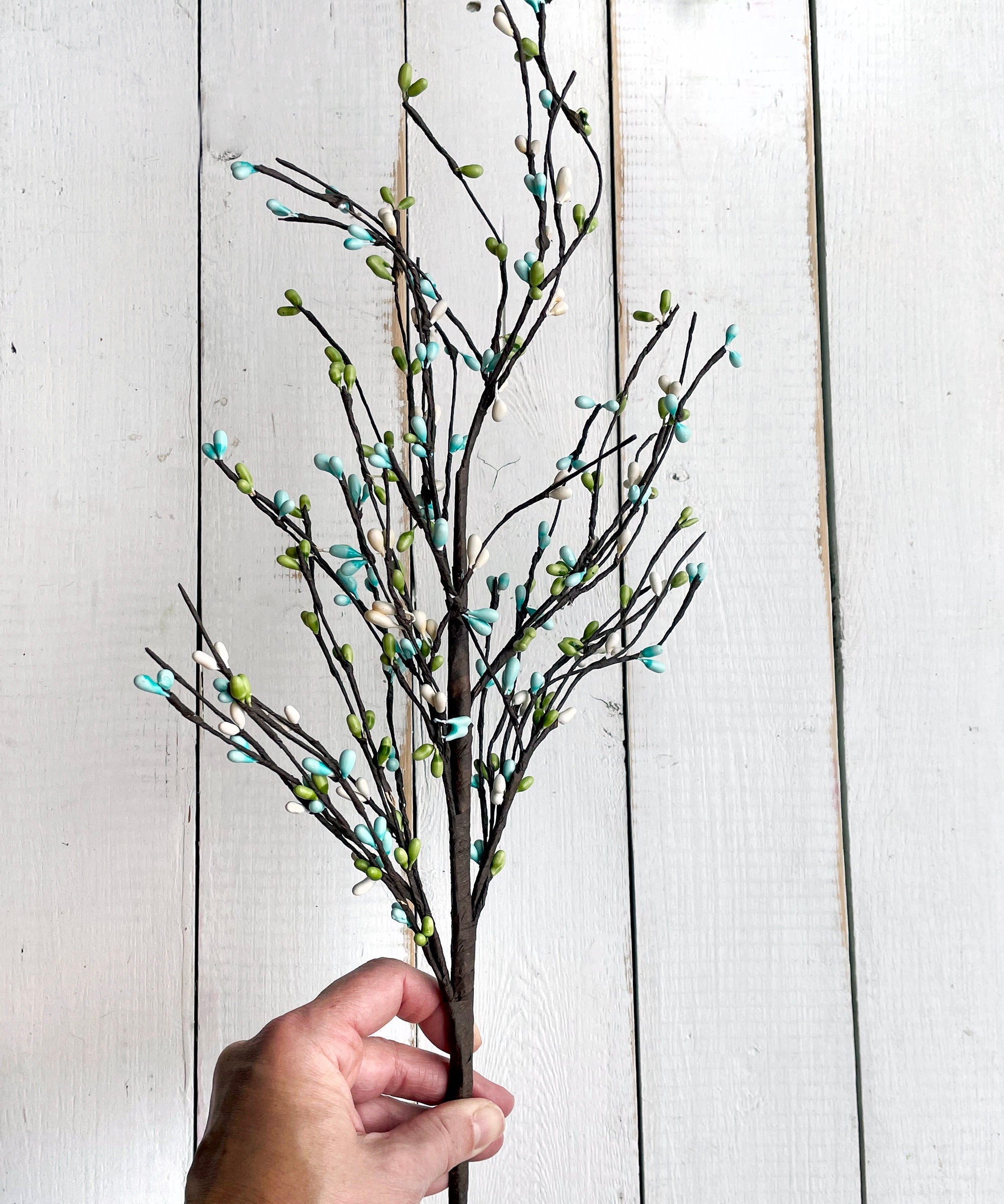 Decorative branch with small blue flowers held by a hand against a light wooden background