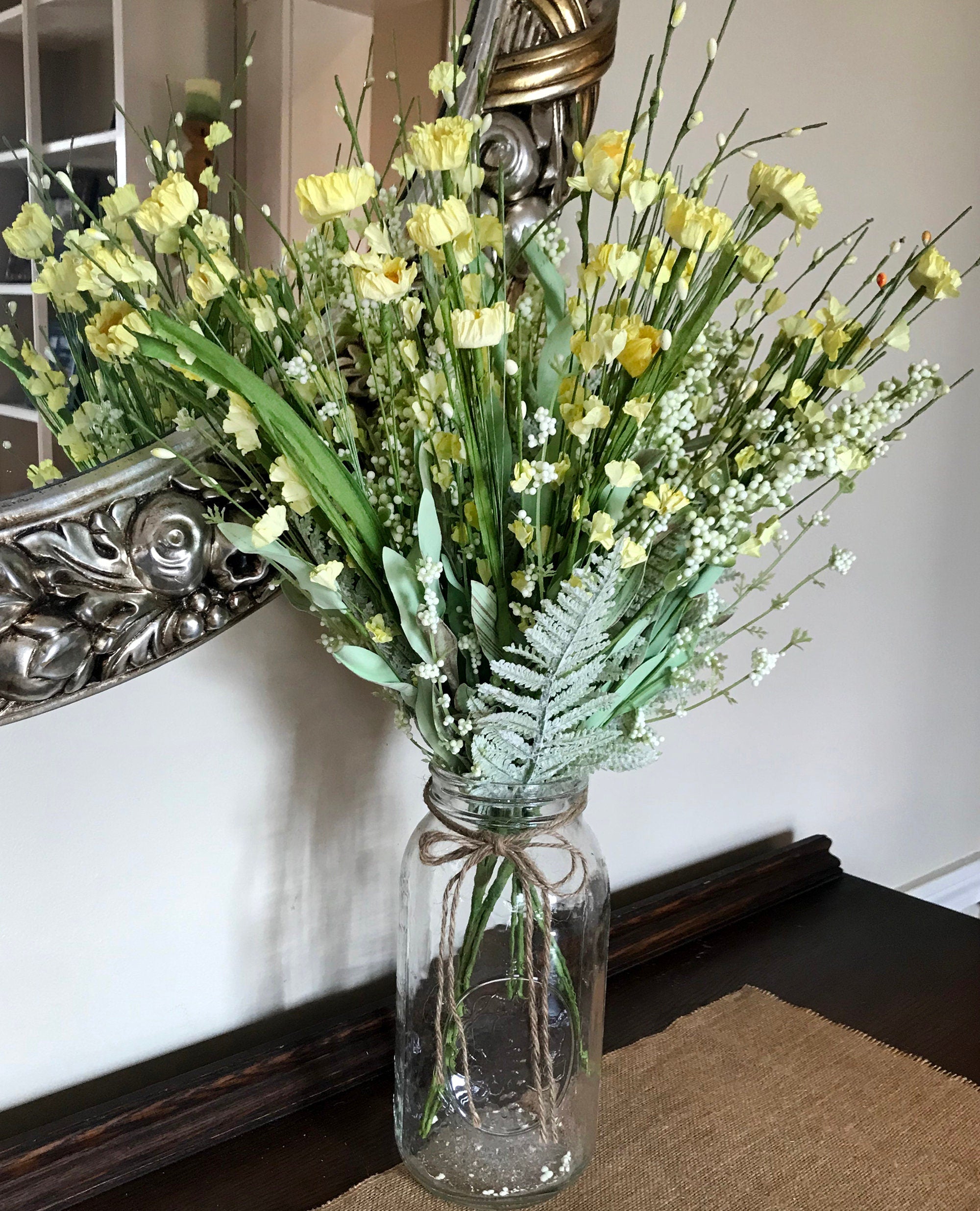 Bouquet of yellow flowers in a clear glass vase on a table with a decorative mirror in the background.