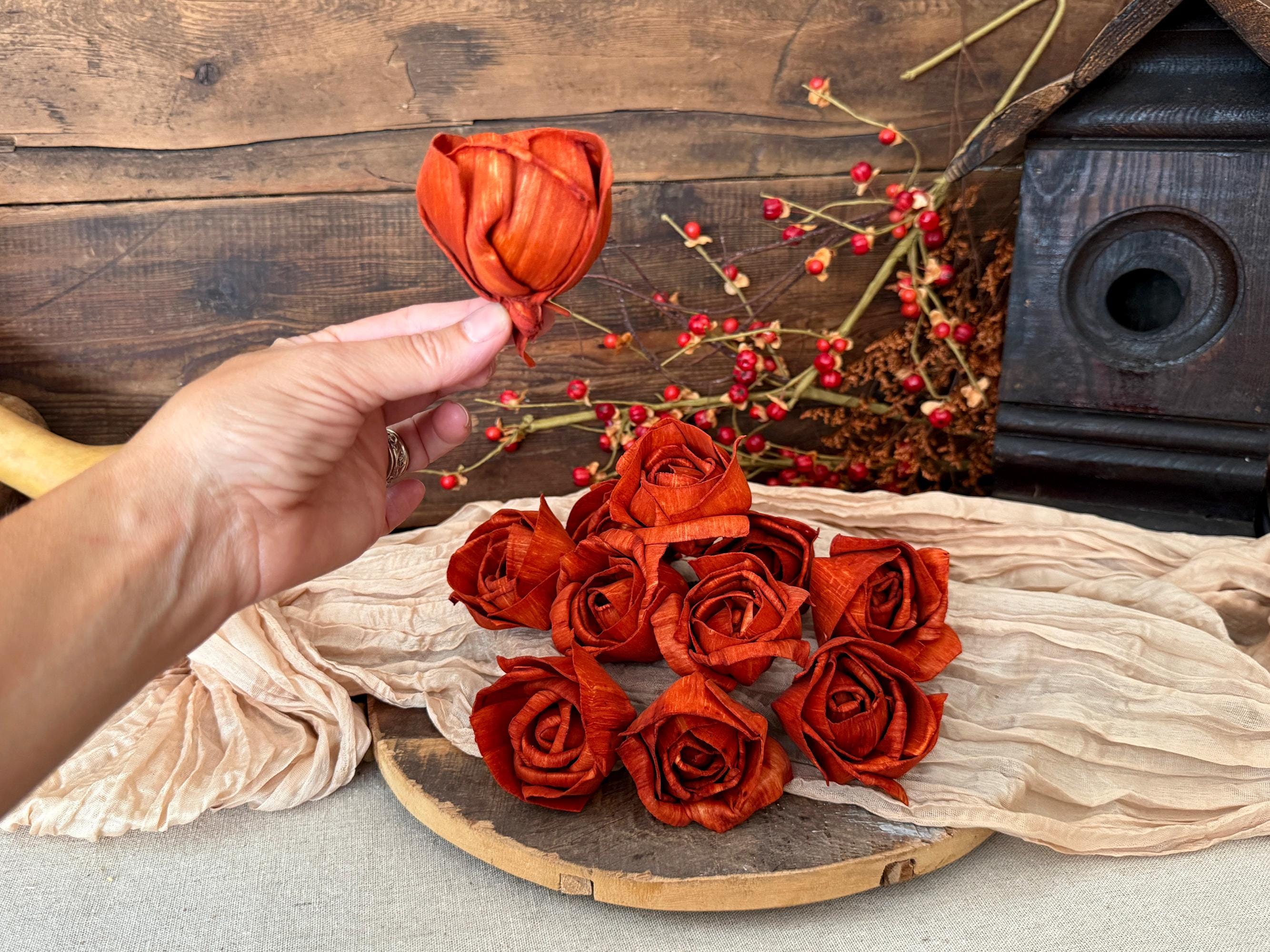 Hand holding a orange rose over a collection of orange roses on a wooden surface.