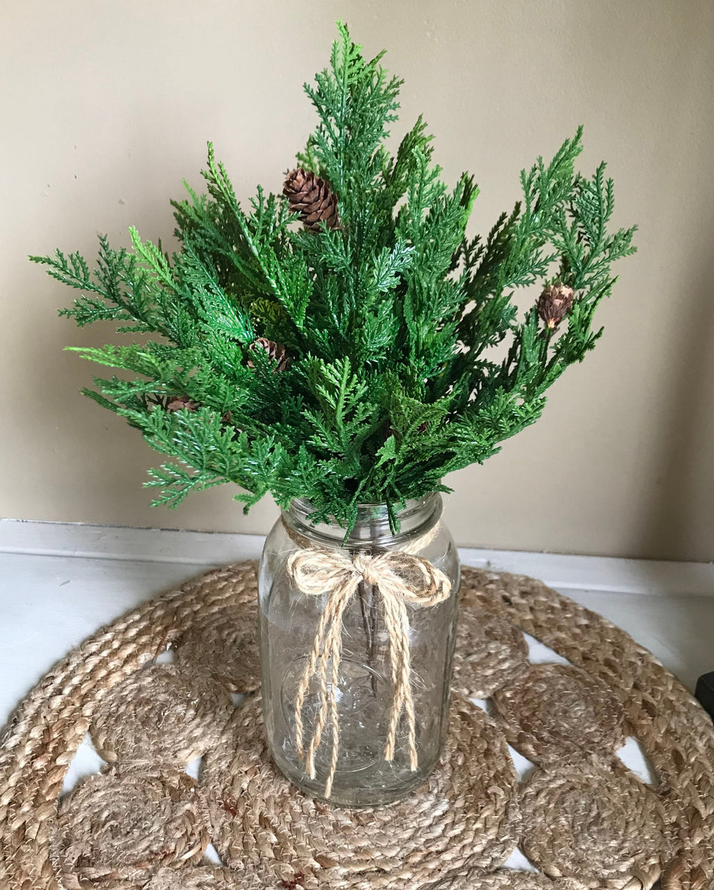 Mason jar with greenery and twine on a woven mat