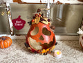 Decorative pumpkin with heart shapes and small figurines on a textured surface with a 'Meet Simon!' sign in the background.