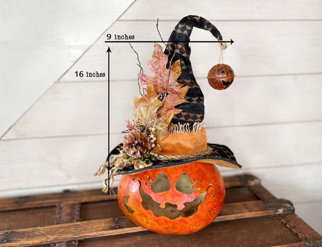 Decorative Halloween pumpkin with witch hat and leaf decorations, placed on a wooden surface.