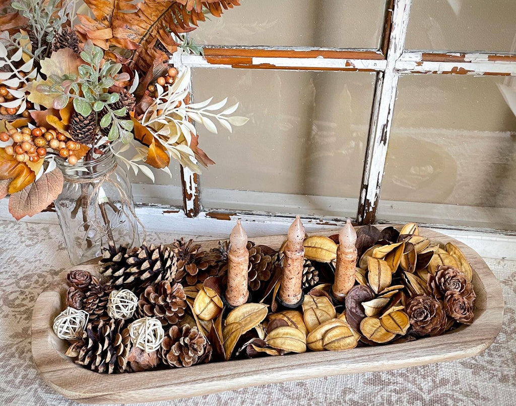 Decorative wood dough bowl display with pinecones, candles, and autumn leaves on a wooden tray.