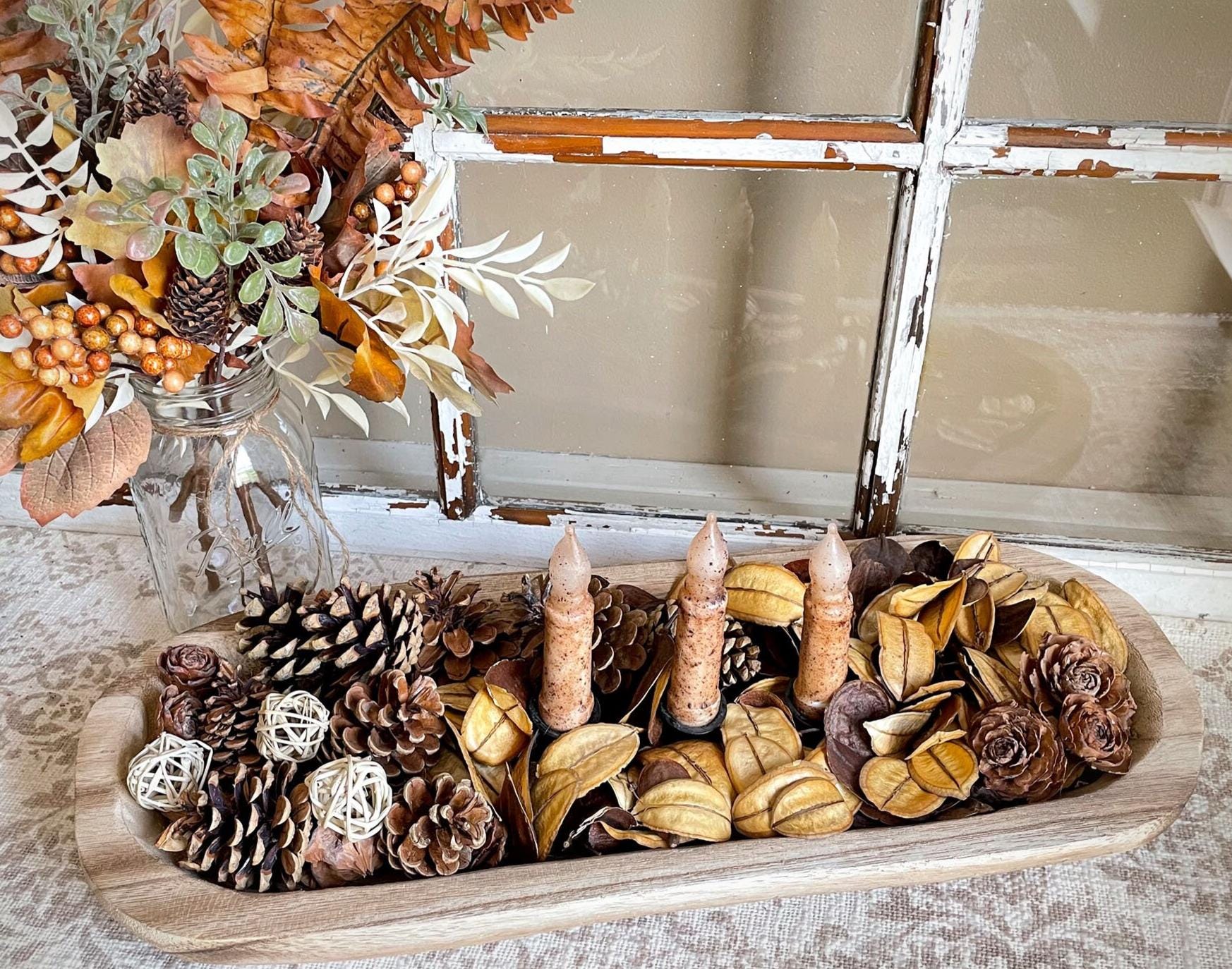 Decorative wood dough bowl display with pinecones, candles, and autumn leaves on a wooden tray.