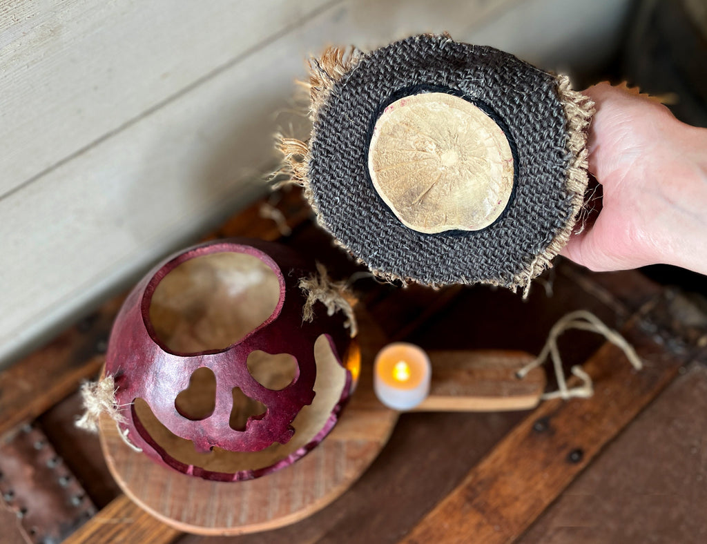 Person holding a textured round object with a candle and half-cut fruit on a wooden surface