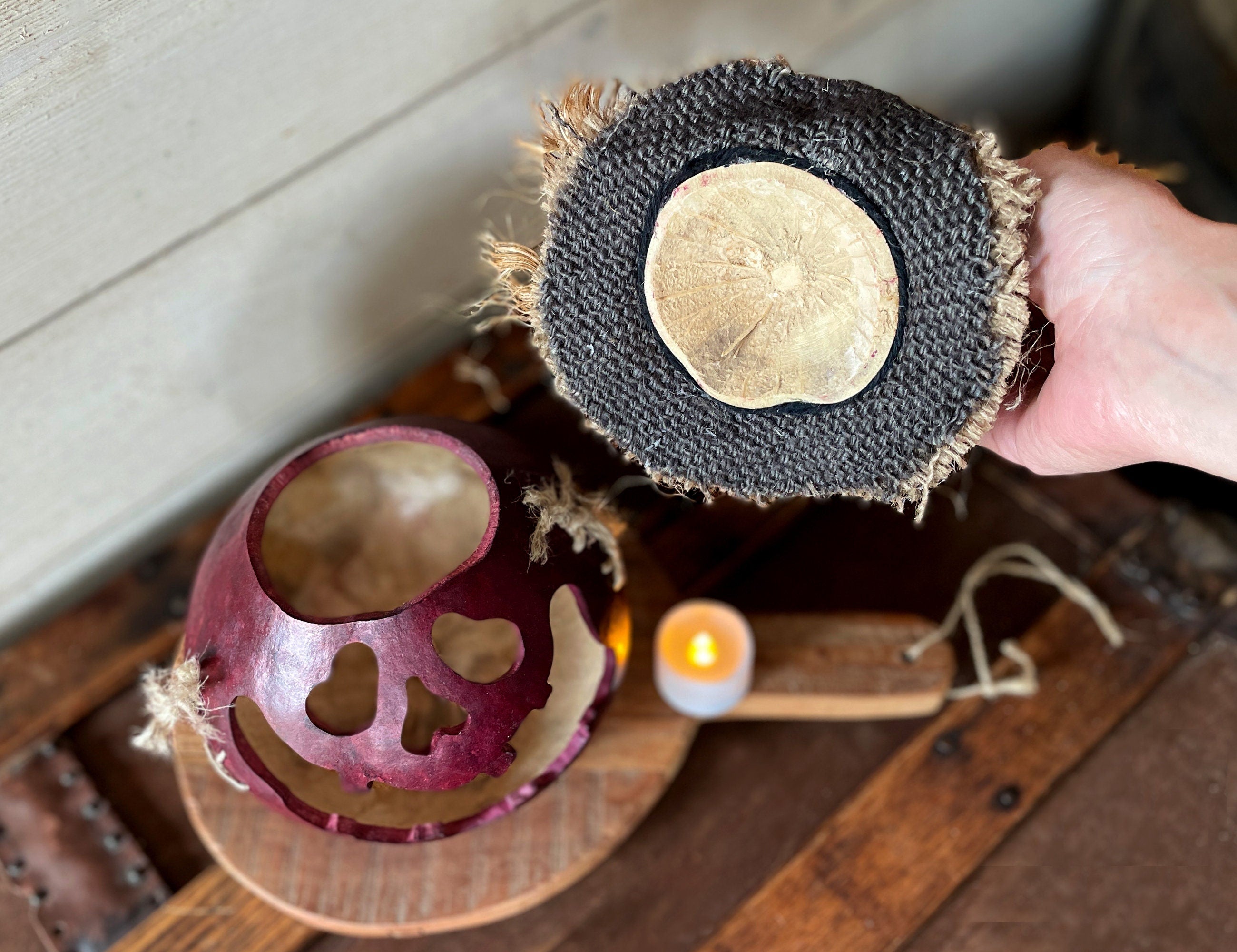 Person holding a textured round object with a candle and half-cut fruit on a wooden surface