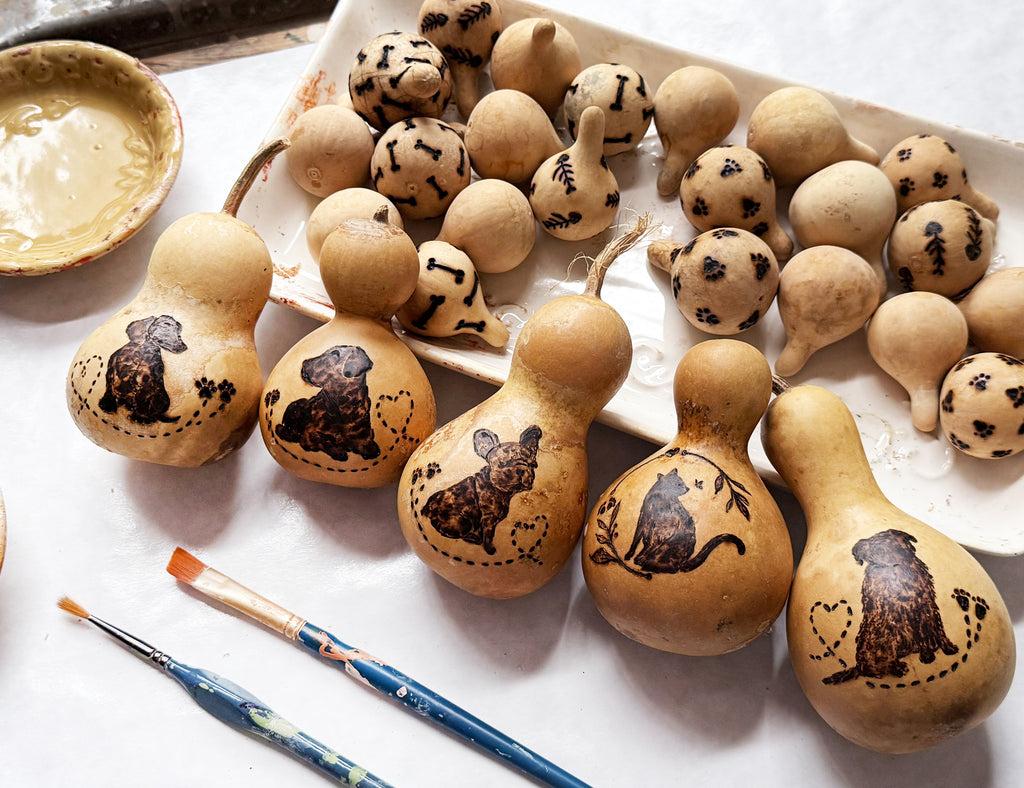 Decorative pet themed gourds with painted designs on a white surface with paintbrushes.