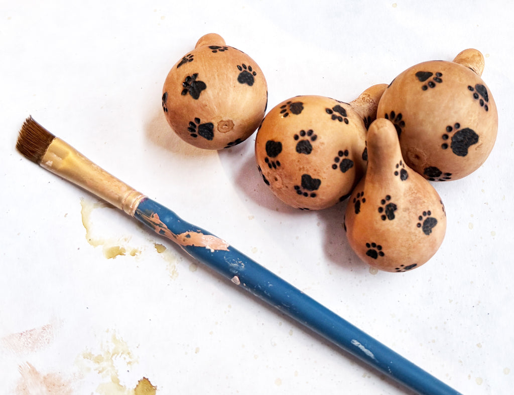 Decorative gourds with paw prints and a paintbrush on a white background