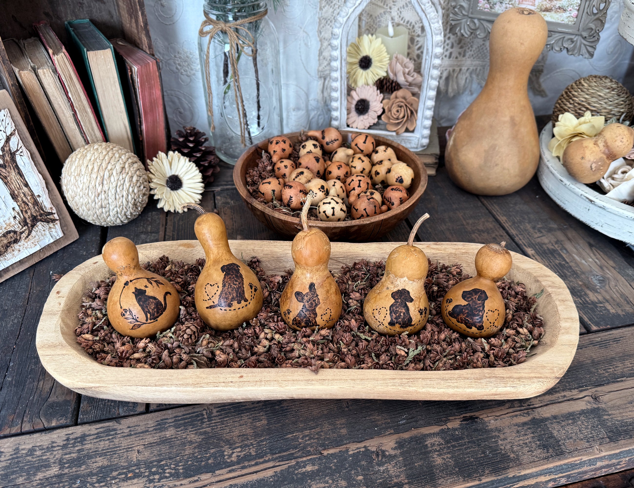 Decorative wooden dough bowl display filled with dried cedar cones with  gourds with hand drawn dogs and cats on them