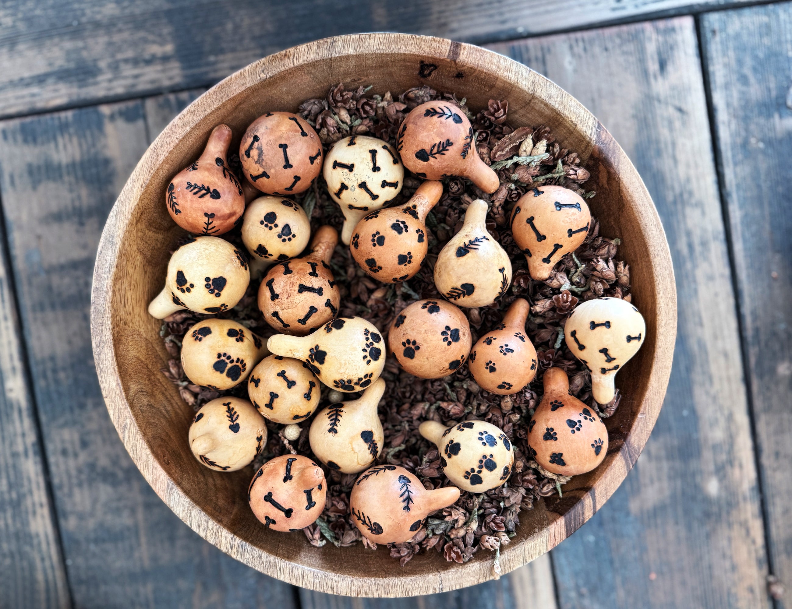 Wooden bowl filled with small decorative pet themed gourds on a wooden surface