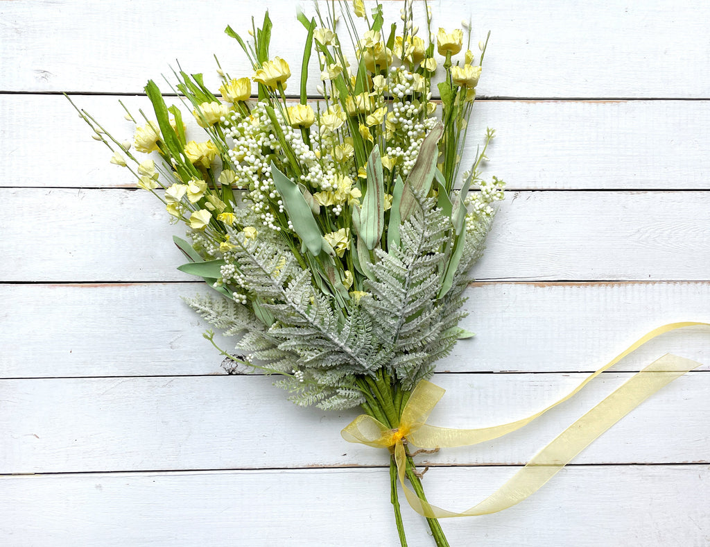 Bouquet of yellow flowers with green leaves on a light wooden surface