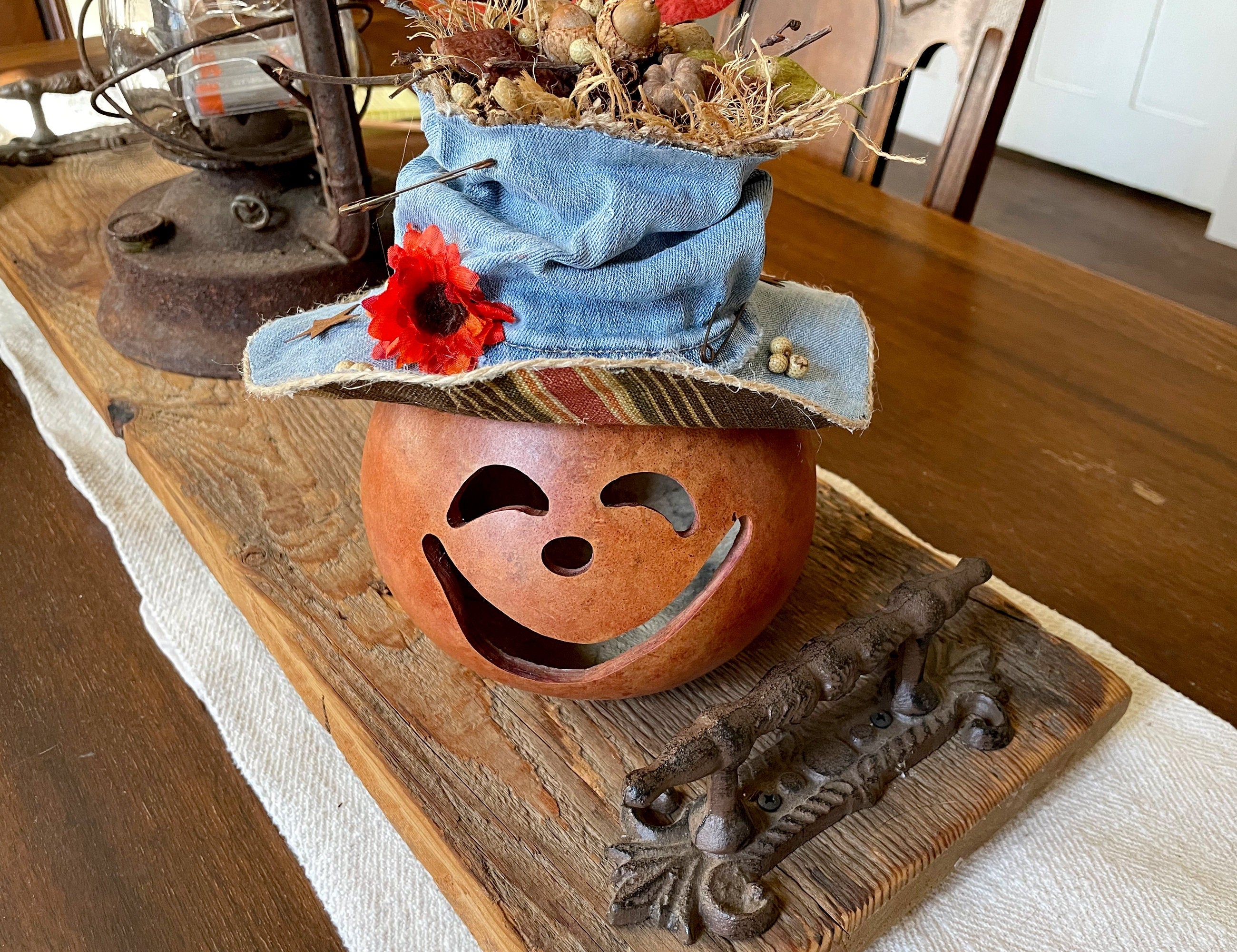 Decorative pumpkin with a denim hat and red flower on a wooden surface