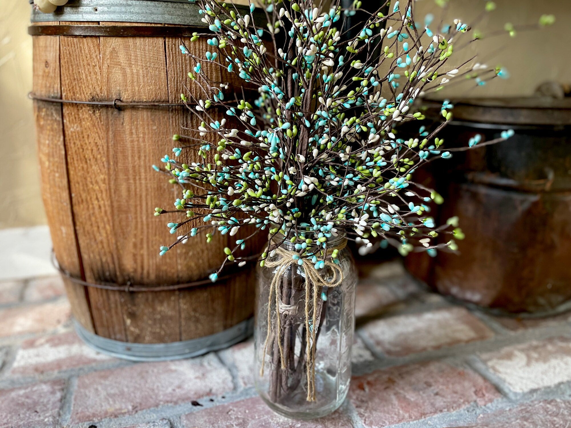 Clear glass vase with decorative branches on a brick surface with wooden barrels in the background