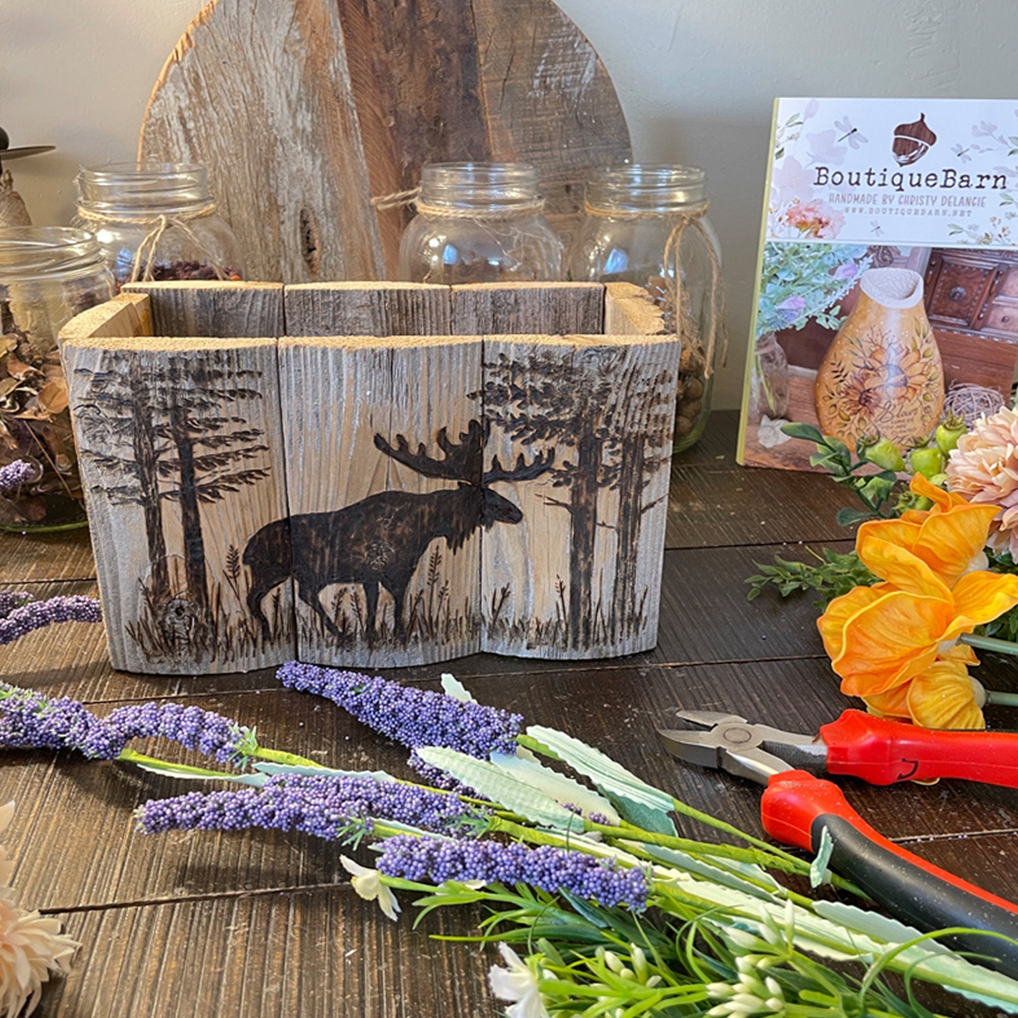 Wooden planter with moose design on a table with flowers and tools