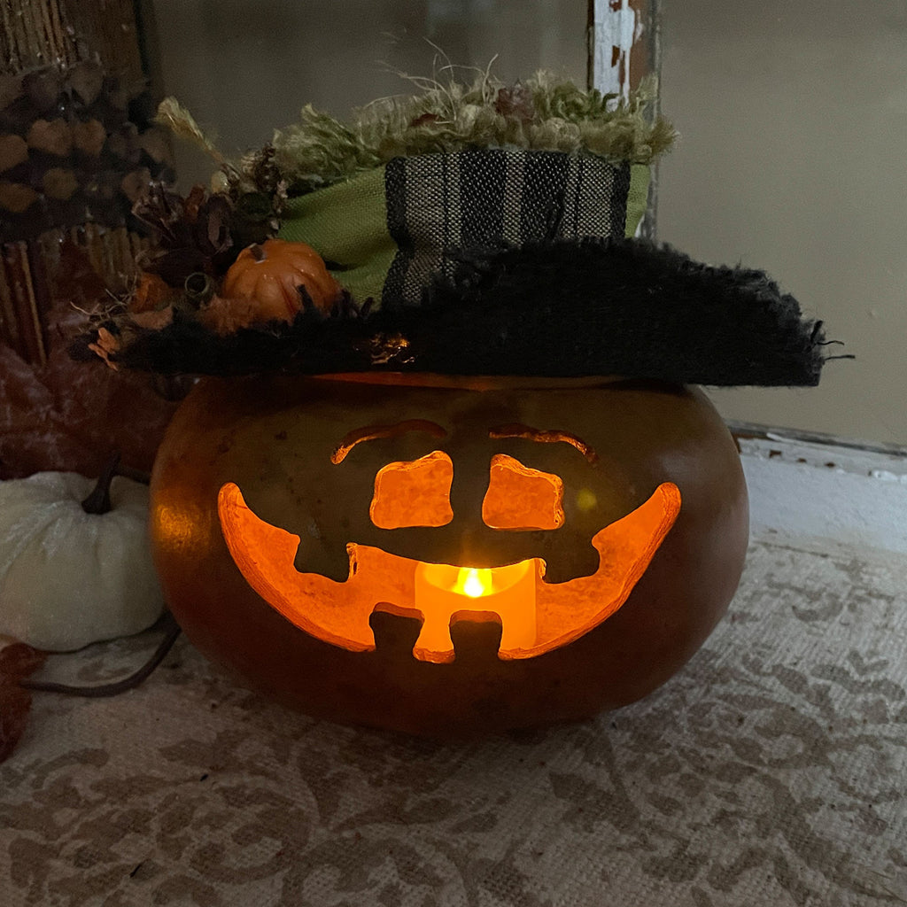 Carved pumpkin with a jack-o'-lantern face on a table with decorative pumpkins in the background.