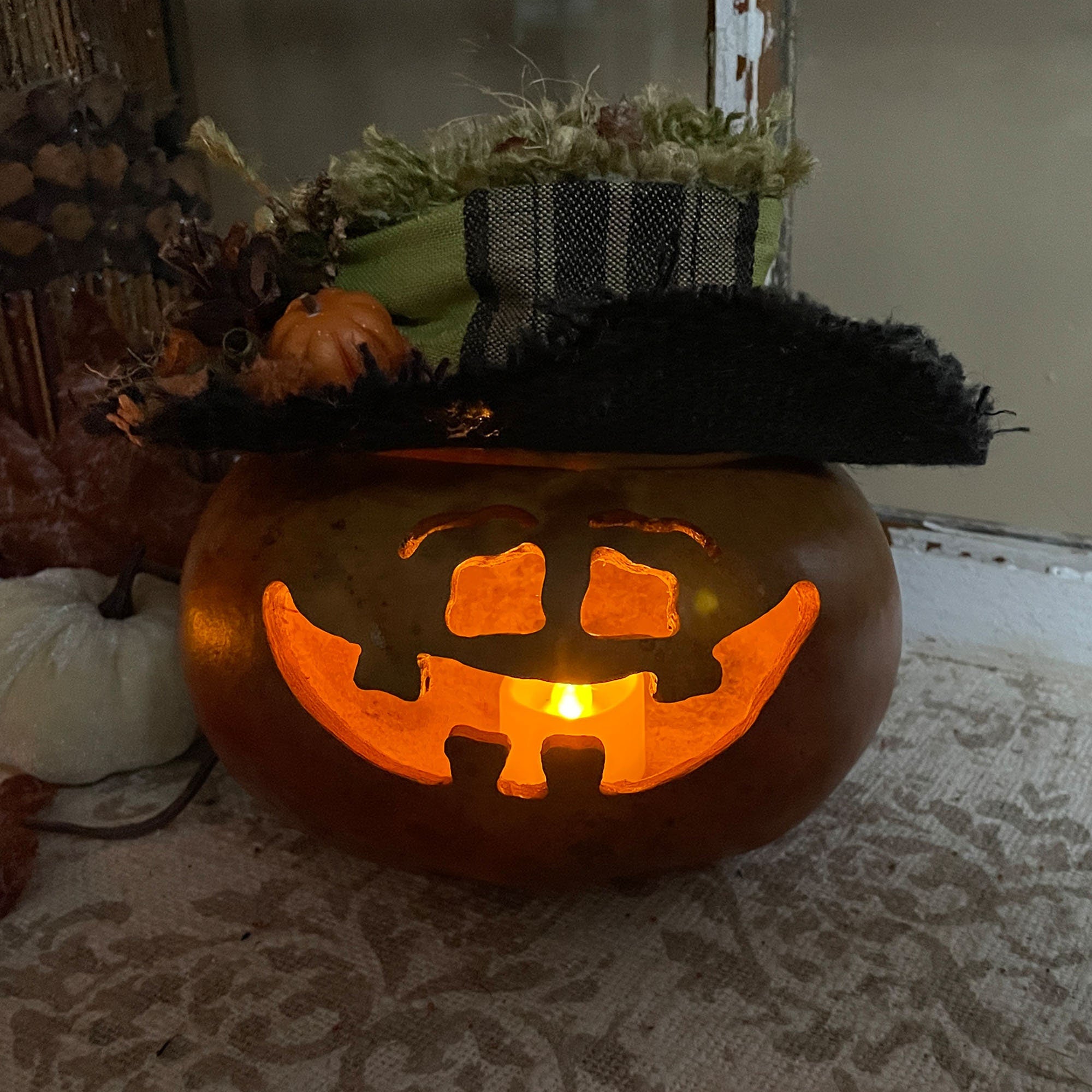 Carved pumpkin with a jack-o'-lantern face on a table with decorative pumpkins in the background.