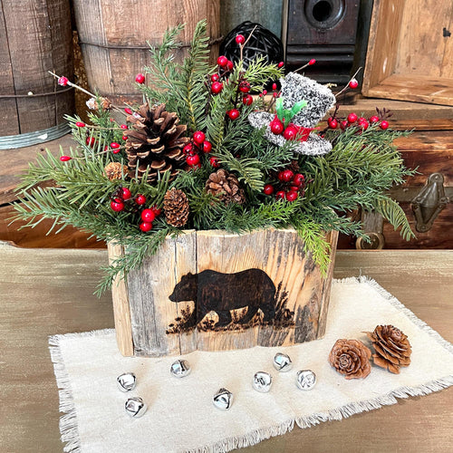 Decorative Christmas arrangement with pinecones and red berries in a wooden box with bear engraving on a rustic background.