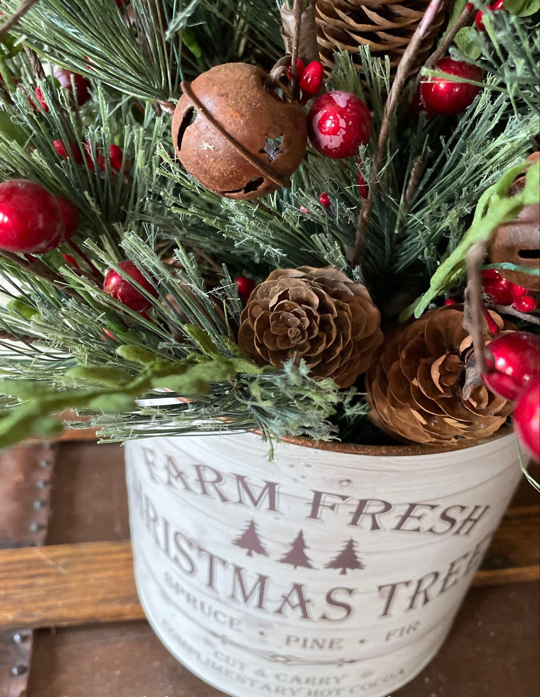 Decorative Christmas arrangement with greenery, red berries, and pinecones in a 'Farm Fresh Christmas Tree' container.