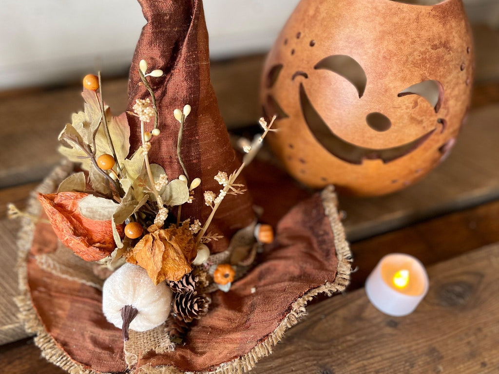 Decorative item with fabric and flowers next to a carved pumpkin and candle on a wooden surface.