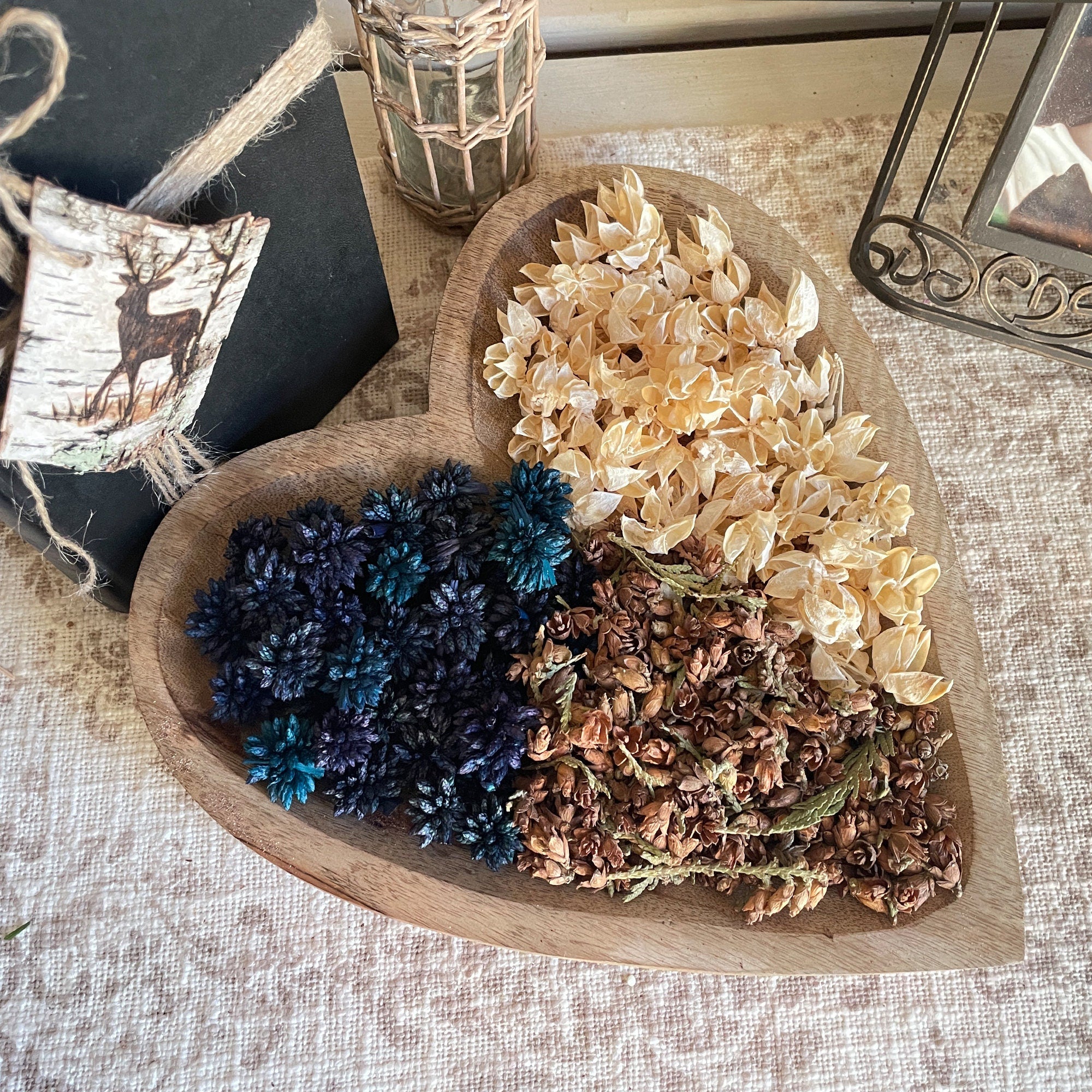 Heart-shaped wooden bowl with dried flowers and leaves on a textured surface