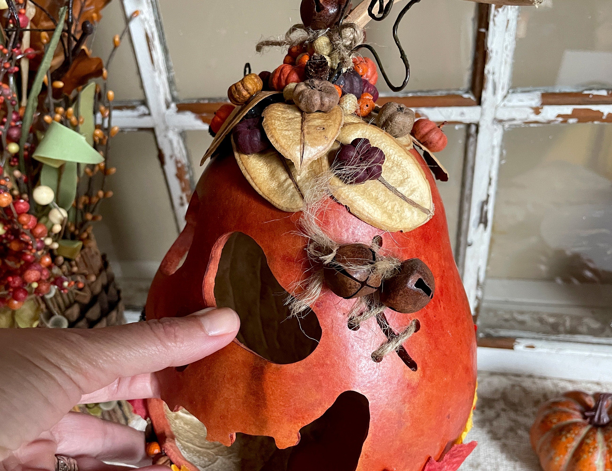 Decorative pumpkin with autumnal elements held by a hand, with a neutral background.