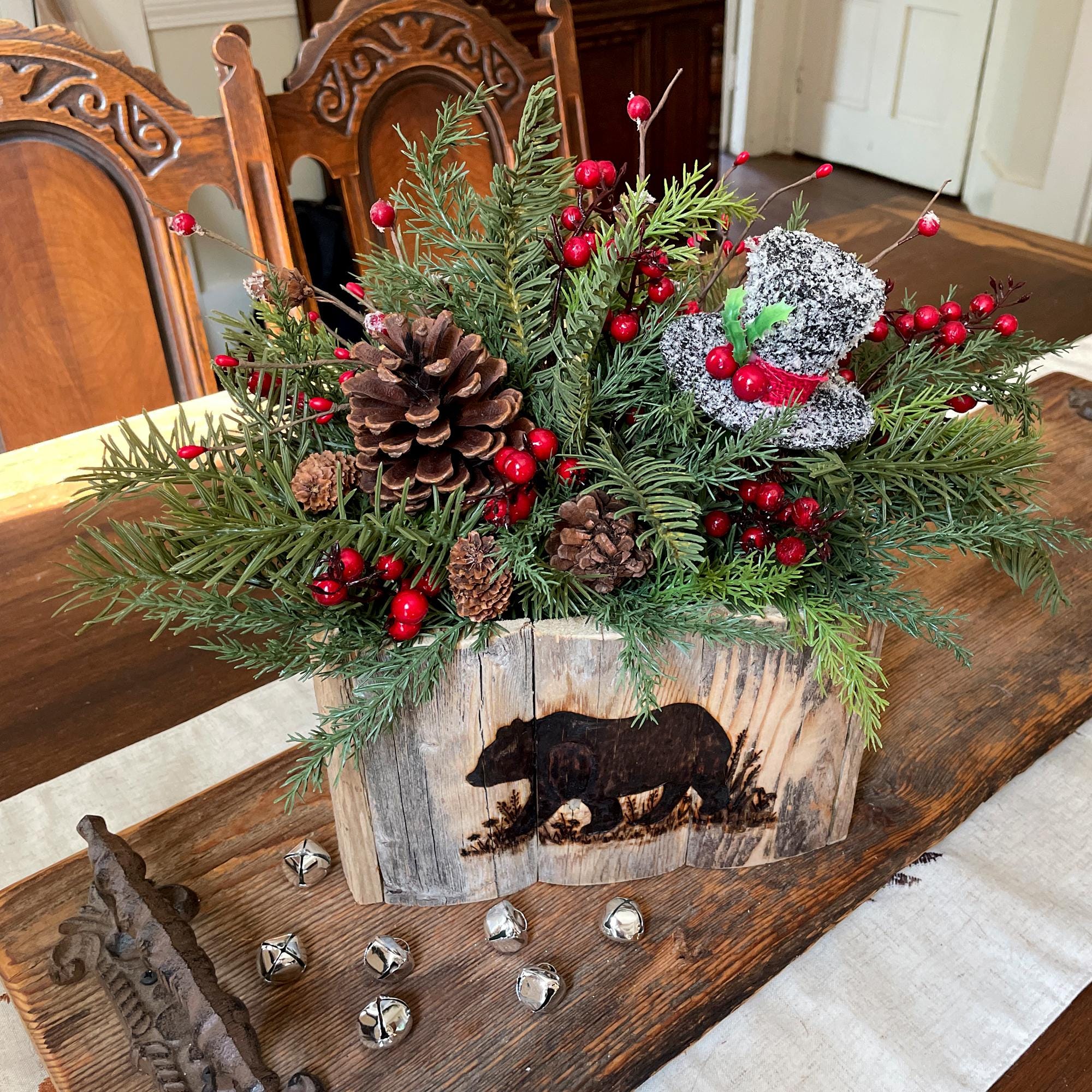 Decorative Christmas arrangement with greenery, pinecones, and red berries on a wooden surface.