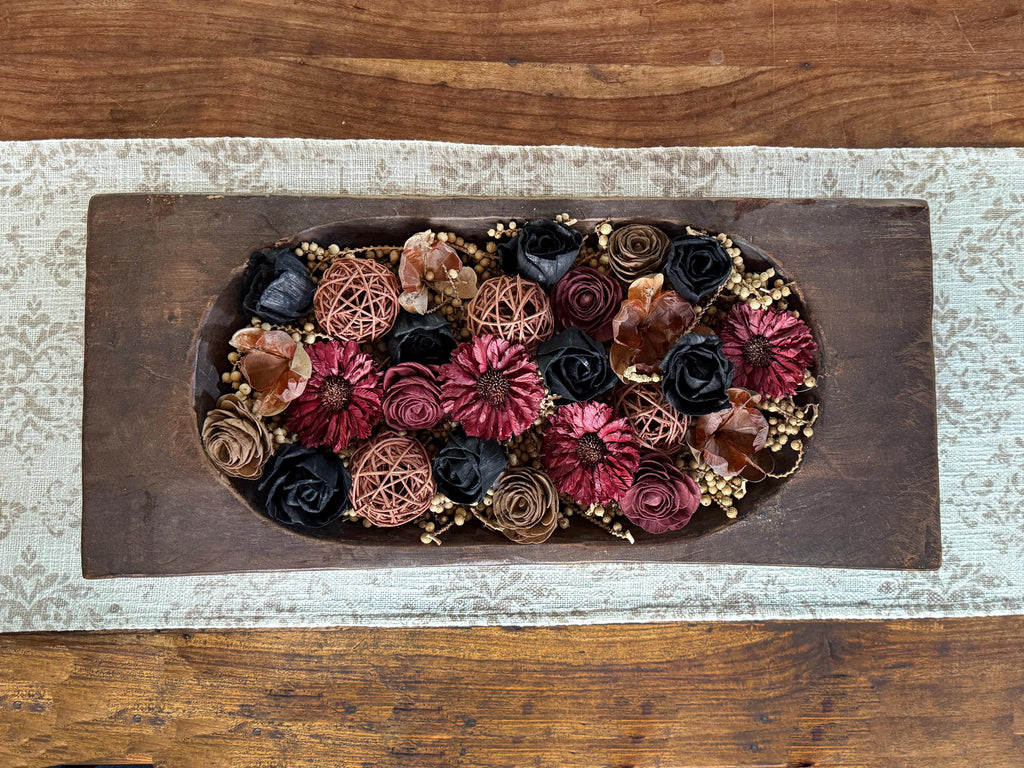 Decorative dough bowl arrangement of dried berries and wood flowers on a wooden coffee table 