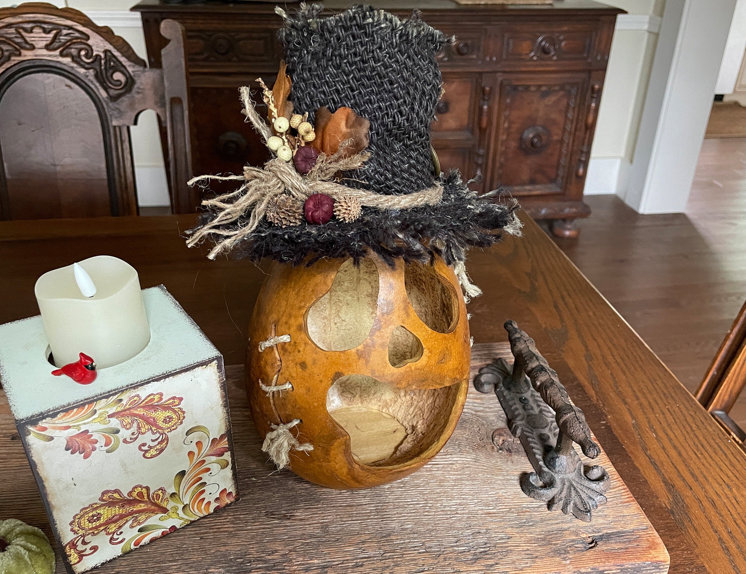 Decorative arrangement with a gourd, candle, and decorative hat on a wooden table.
