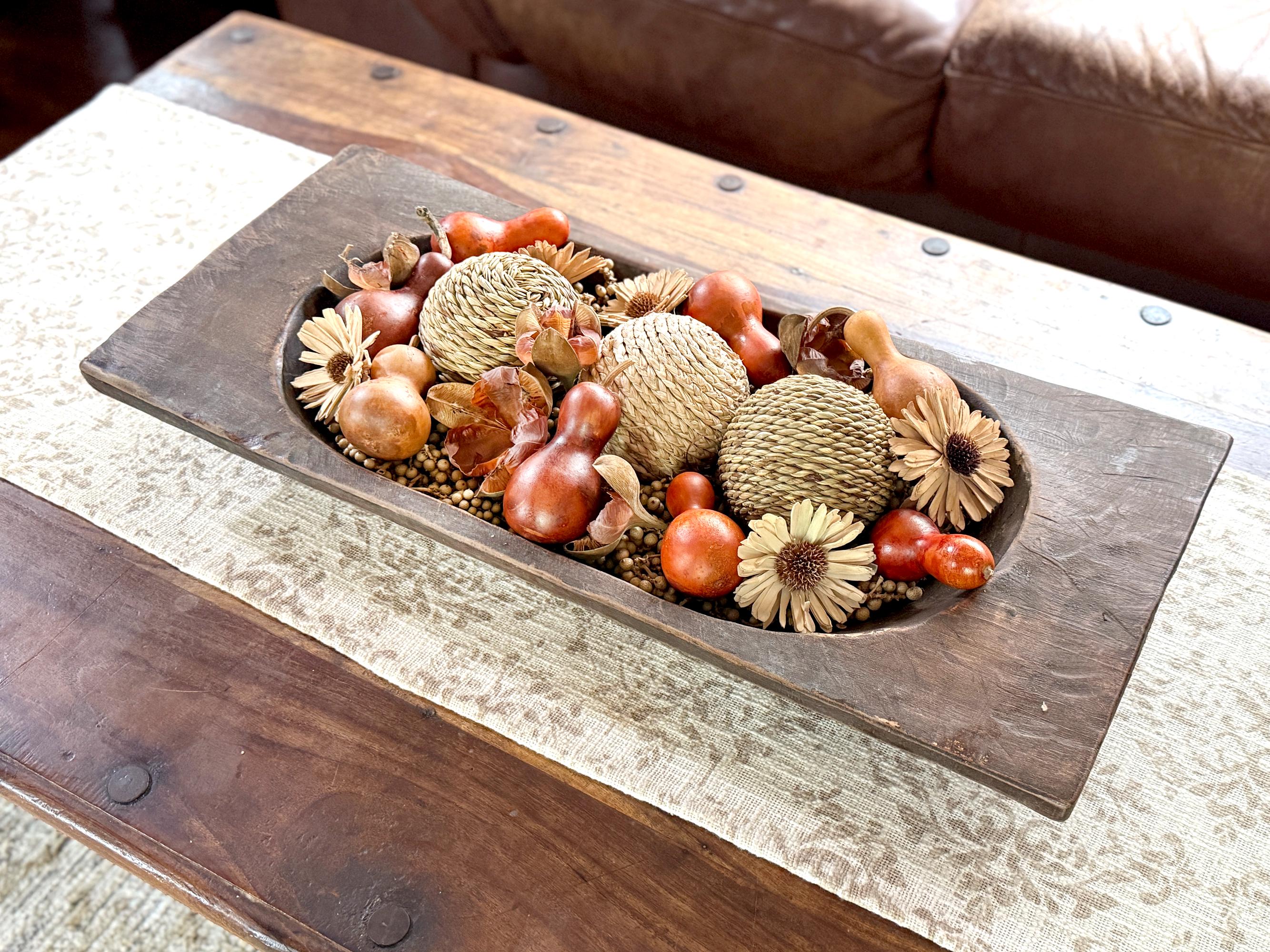 Decorative arrangement of gourds and pumpkins in a wooden bowl on a coffee table.