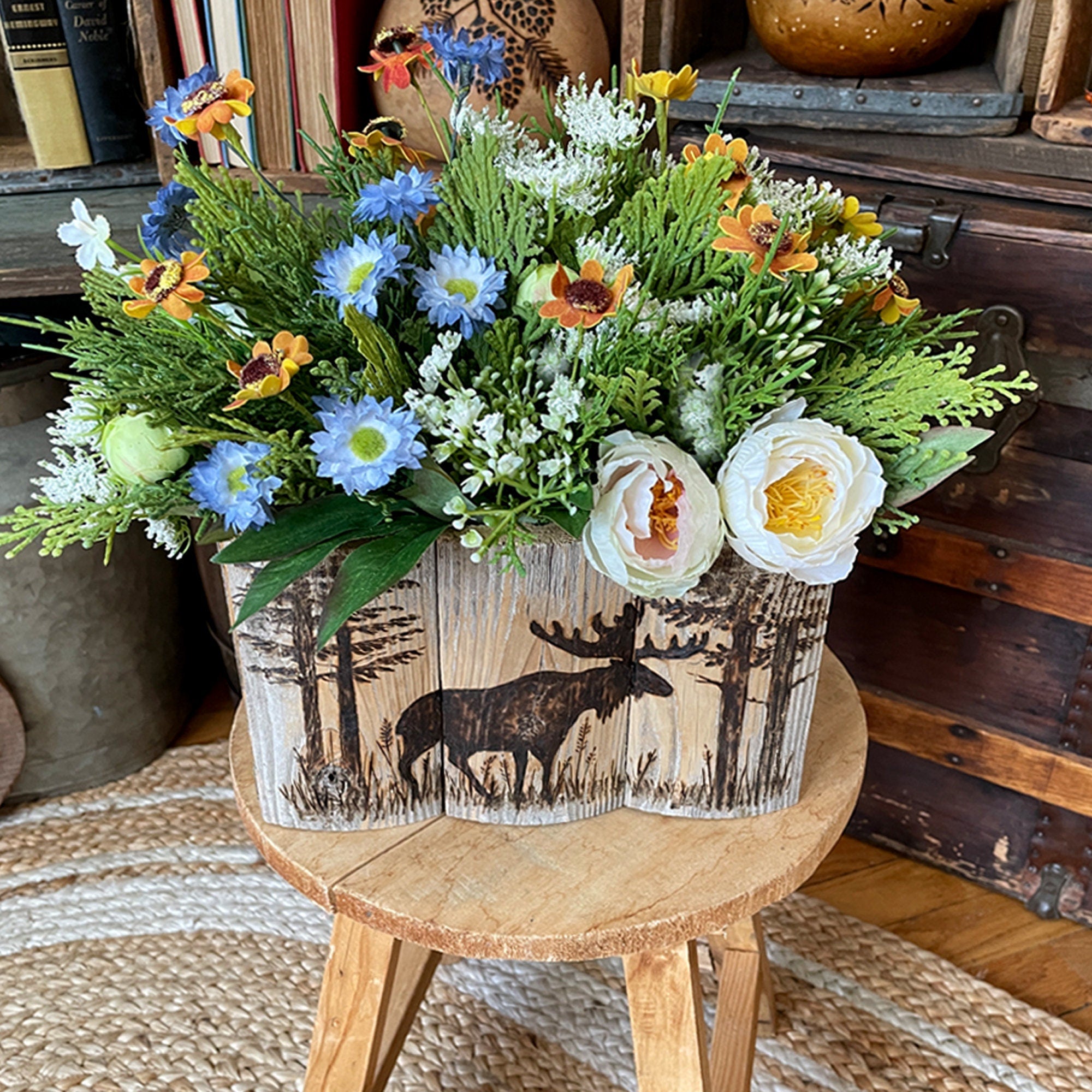 Floral arrangement in a wooden container with moose design on a small wooden stool.