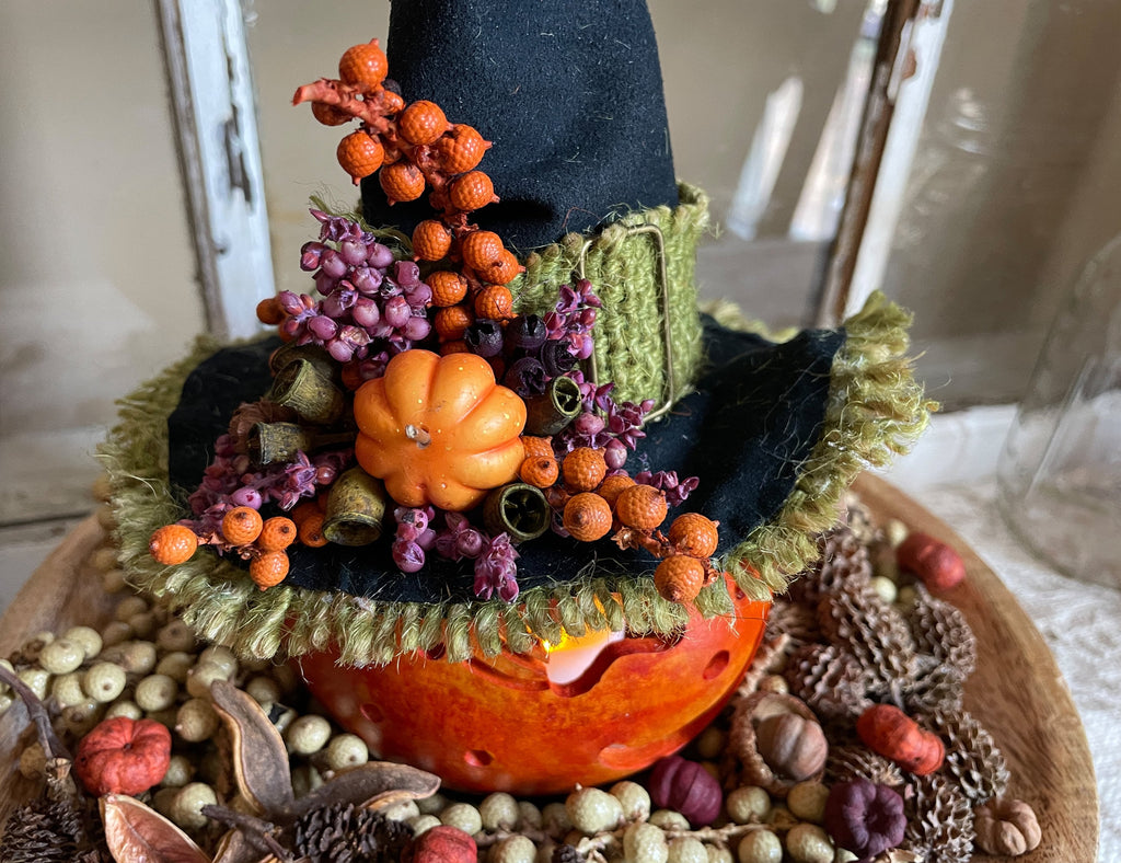 Decorative pumpkin with a witch hat and autumnal elements on a wooden surface.