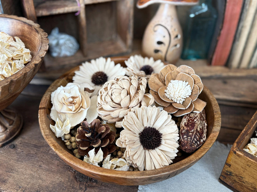 Wooden bowl filled with decorative flowers and pinecones on a wooden surface.