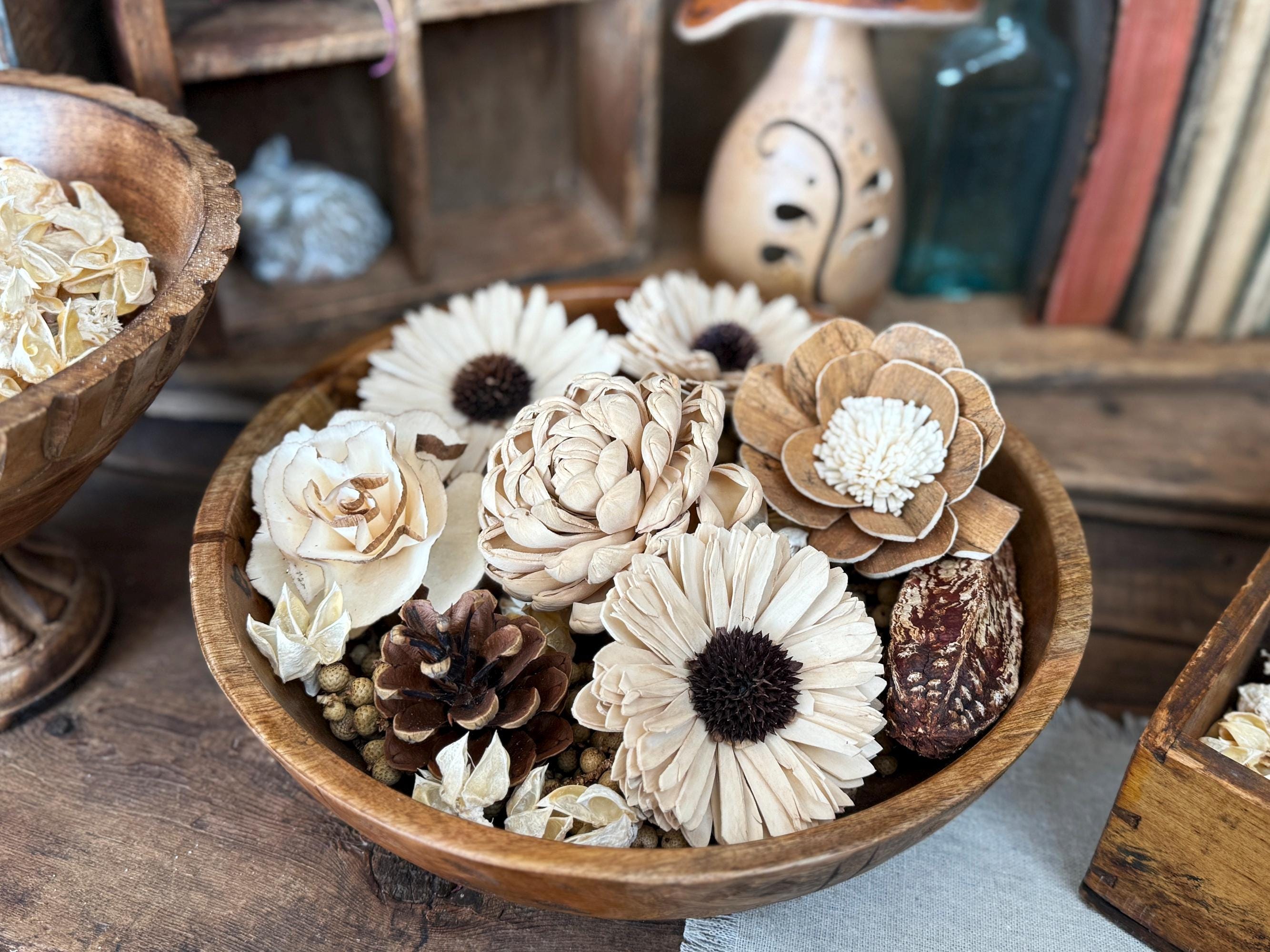Wooden bowl filled with decorative flowers and pinecones on a wooden surface.
