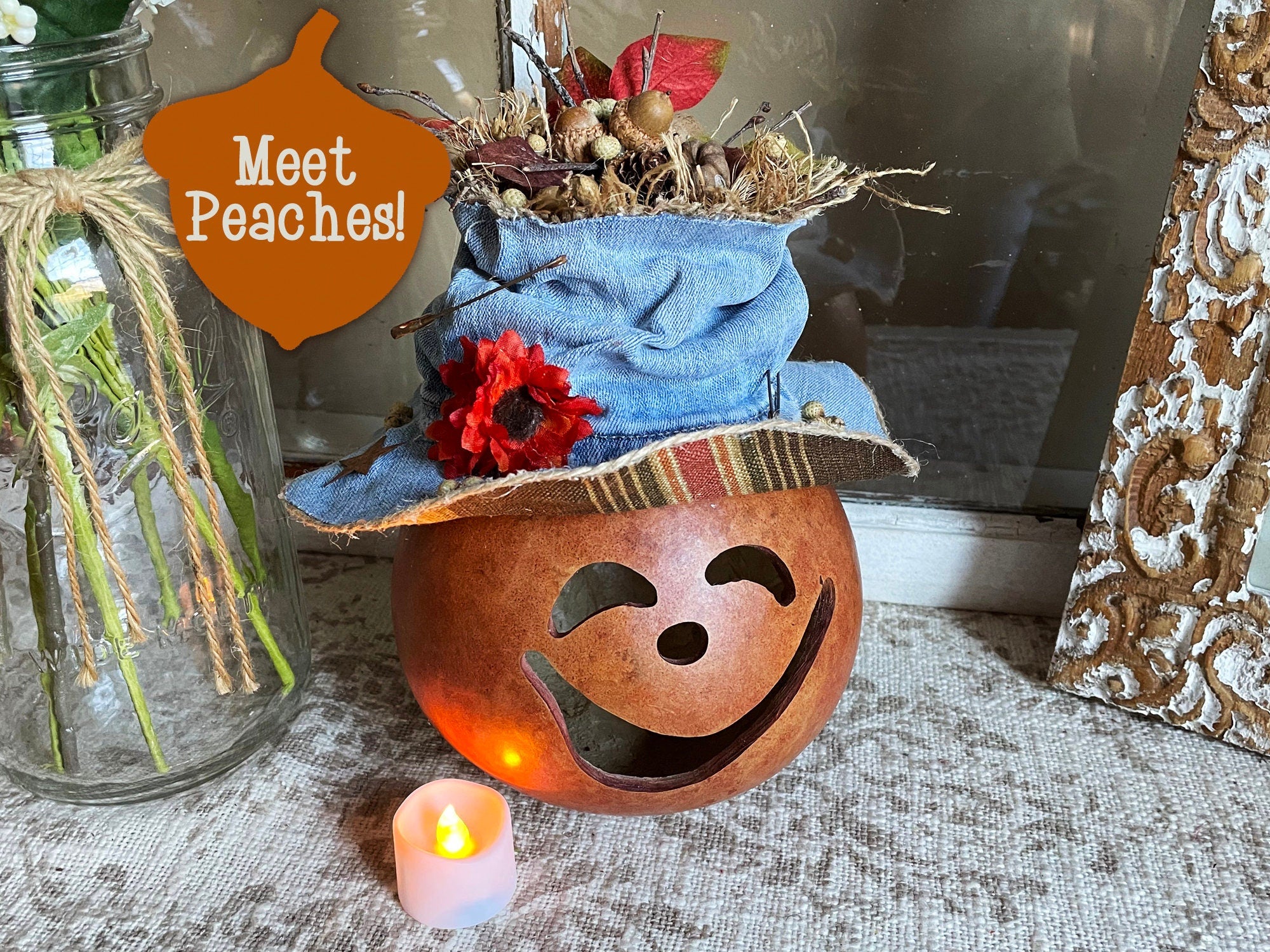 Decorative pumpkin with a face and blue hat, lit candle, and 'Meet Peaches!' sign.