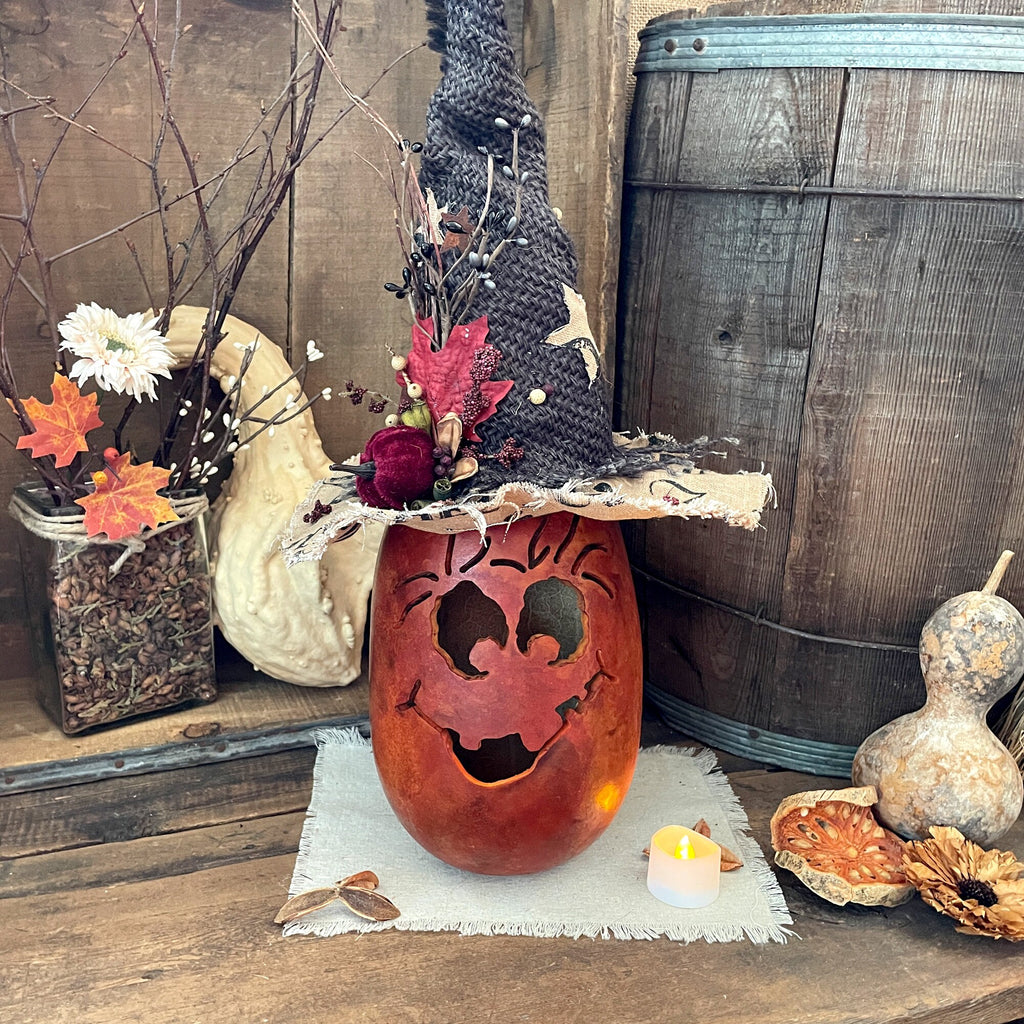 Decorative setup with a carved pumpkin, flowers, and gourds on a wooden surface.