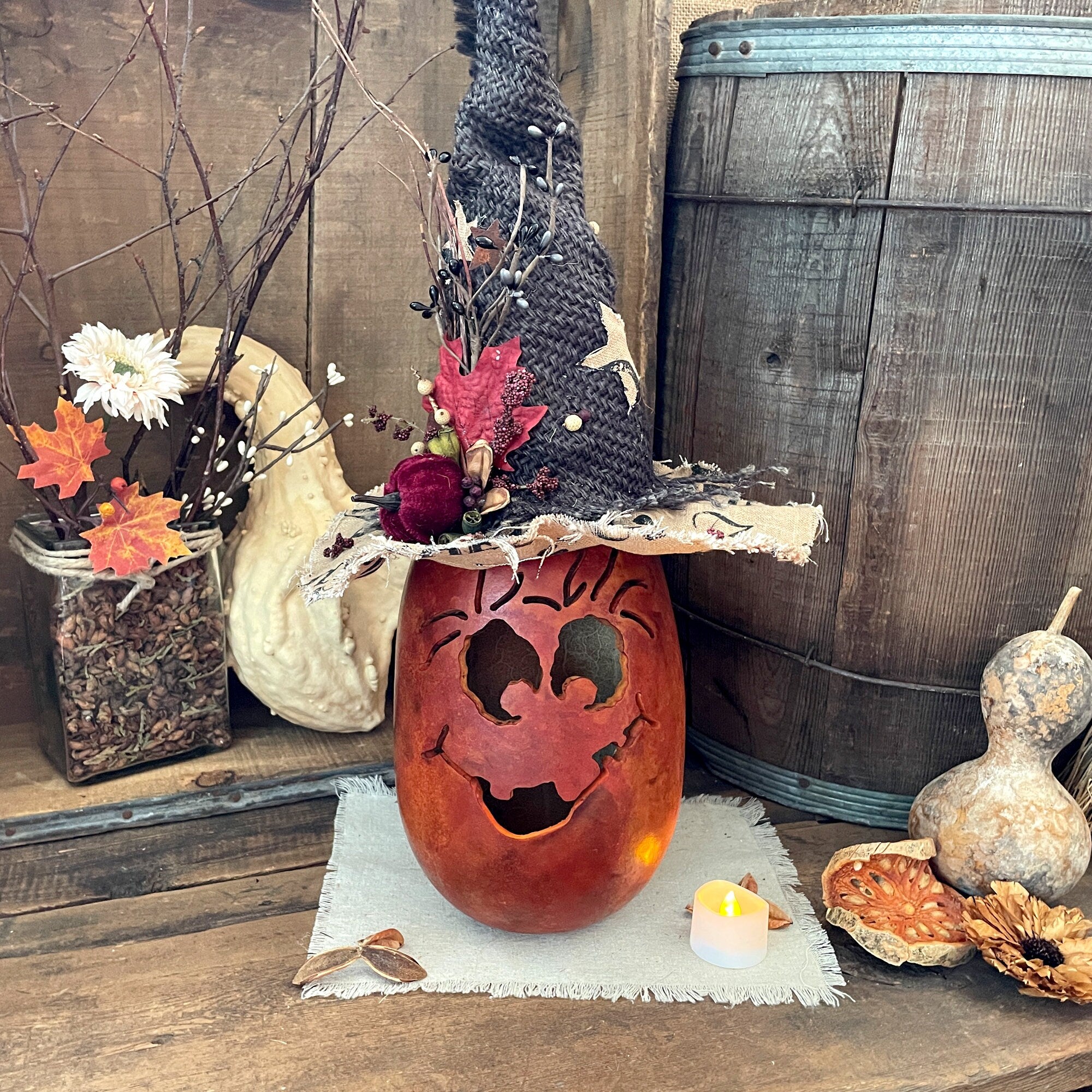 Decorative setup with a carved pumpkin, flowers, and gourds on a wooden surface.
