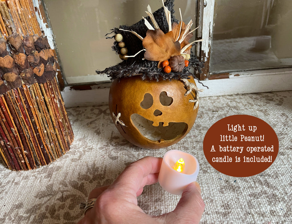 Decorative pumpkin with a face, lit by a battery-operated candle, on a textured surface.