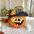 Decorative pumpkin with a witch hat and small pumpkins on a textured surface.