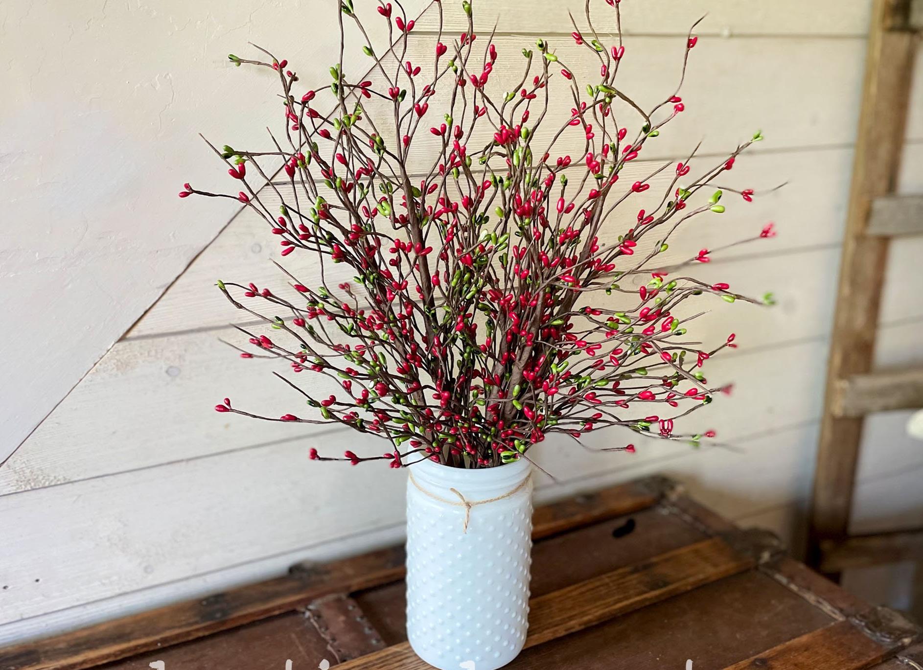 White milk glass vase with red and green floral arrangement on a wooden surface.