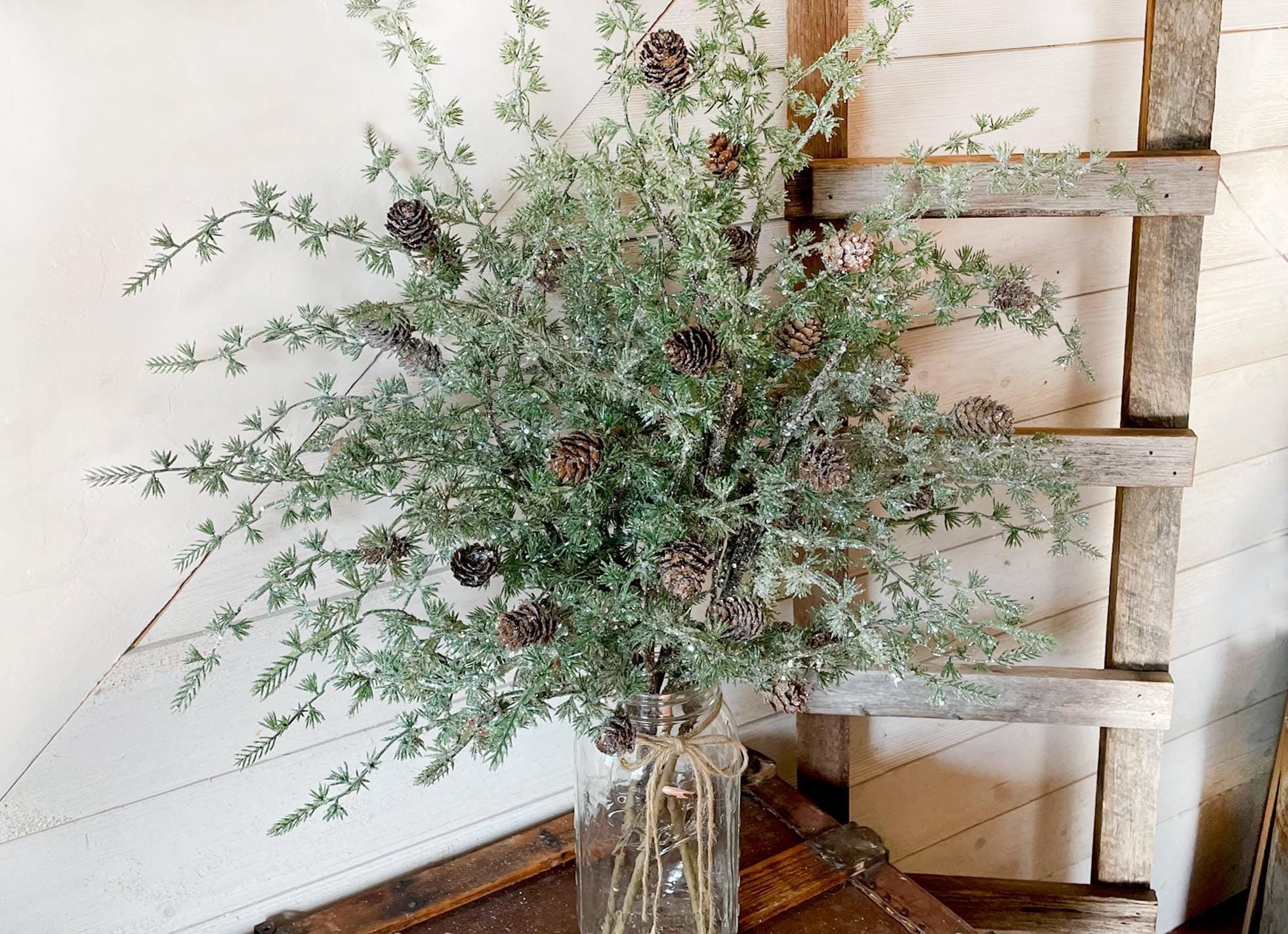 Bouquet of iced greenery with pinecones in a clear vase on a wooden pallet.