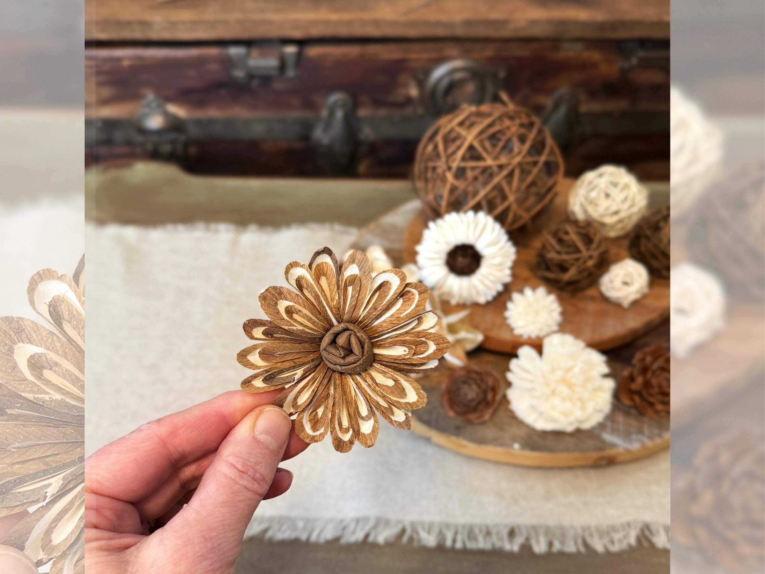 Gold flower-shaped object held by a hand with decorative flowers and a wooden box in the background.